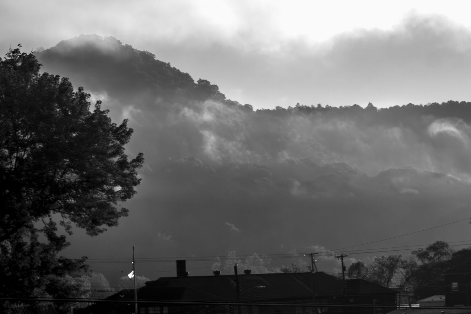Dark storm clouds gather over a mountainous landscape at dusk.