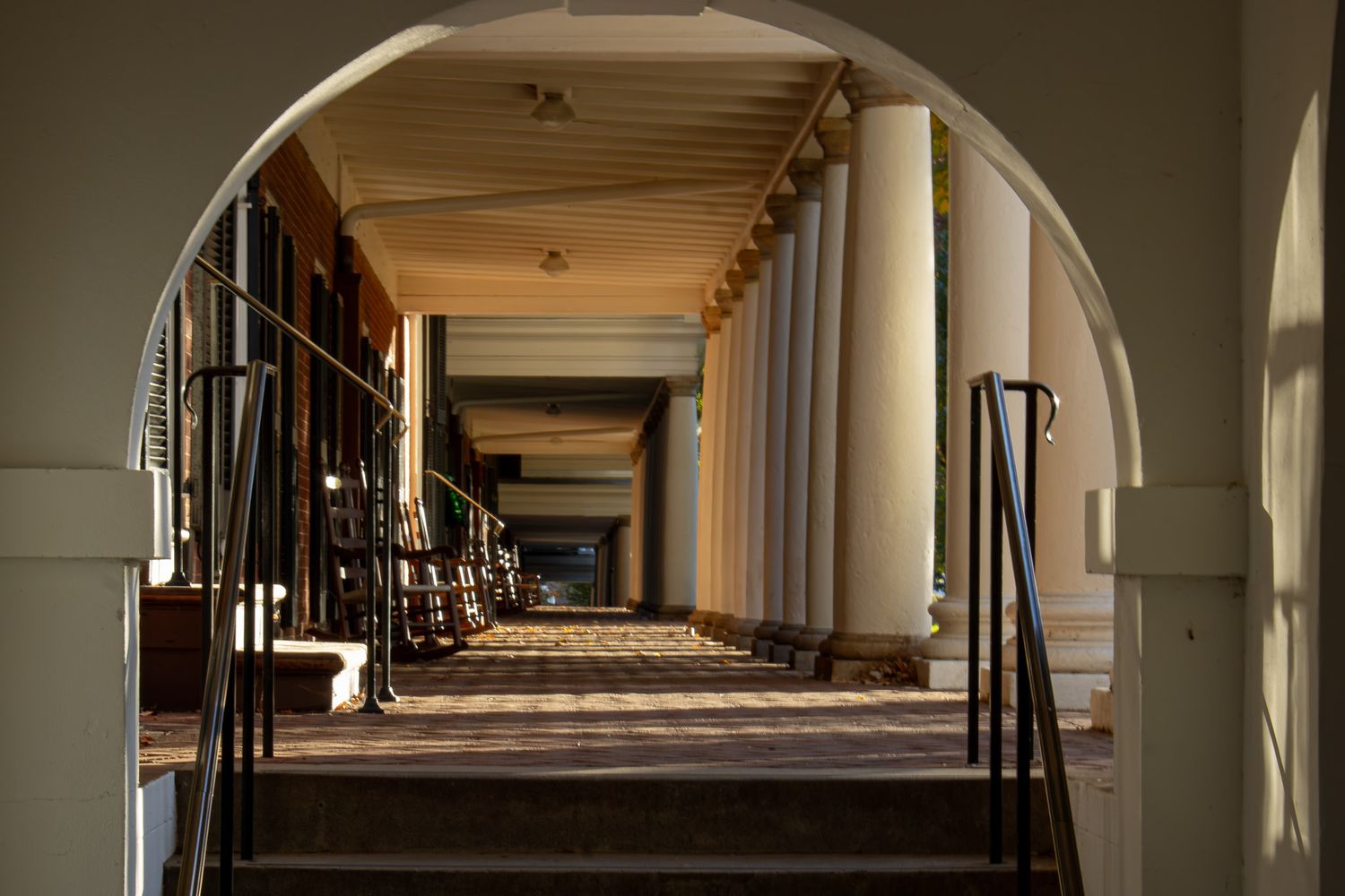 Sunlit colonnade with repeating arches and columns creating dramatic shadows and perspective.