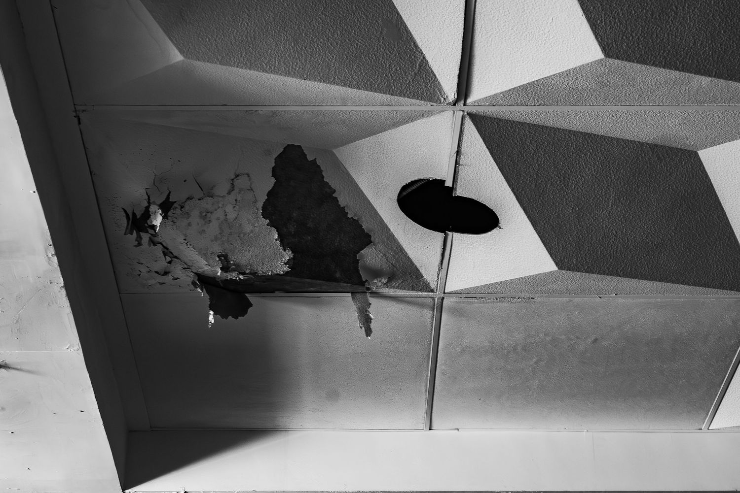 Abstract geometric ceiling pattern with hole and shadow in black and white.