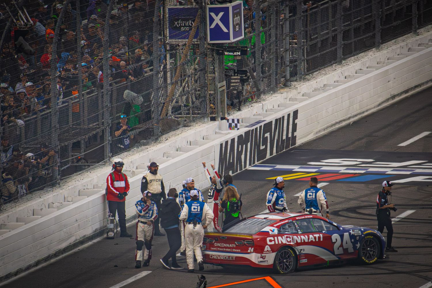 Safety team members surround damaged race car during NASCAR event.