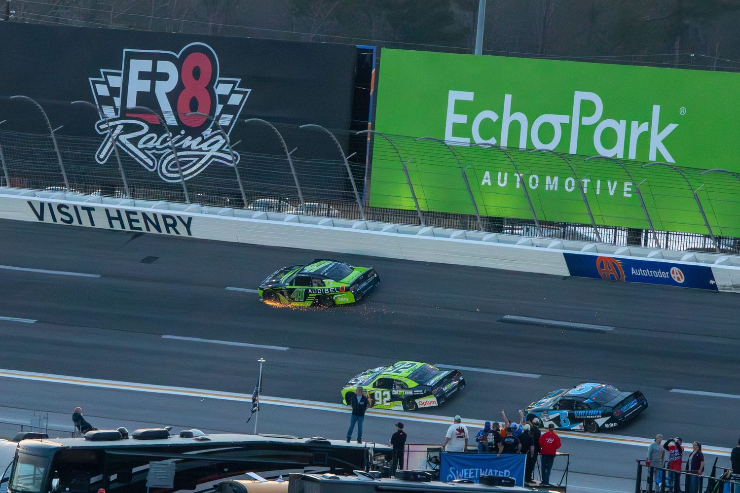Race cars speed past EchoPark Automotive signage during the Bennet Transportation & Logistics 250