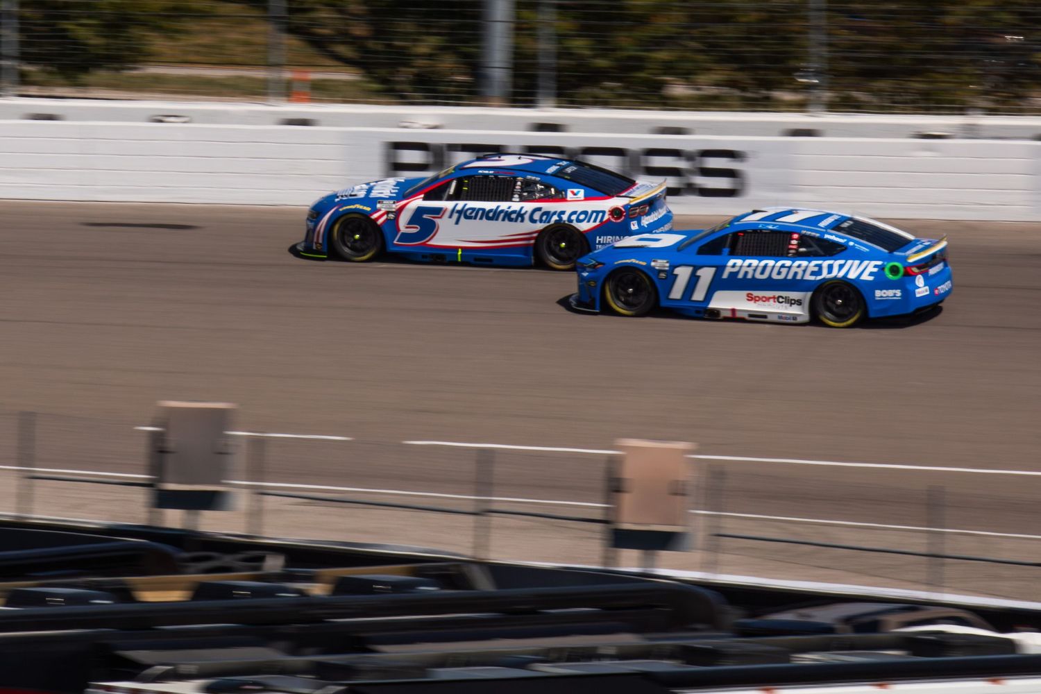 Blue and white NASCAR vehicles compete for position on the racetrack.