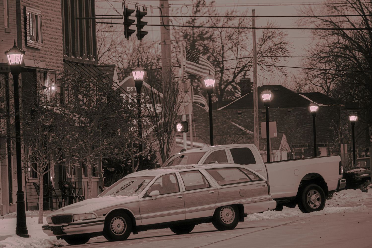 Vintage sepia photograph of parked cars and street lamps along an urban street.