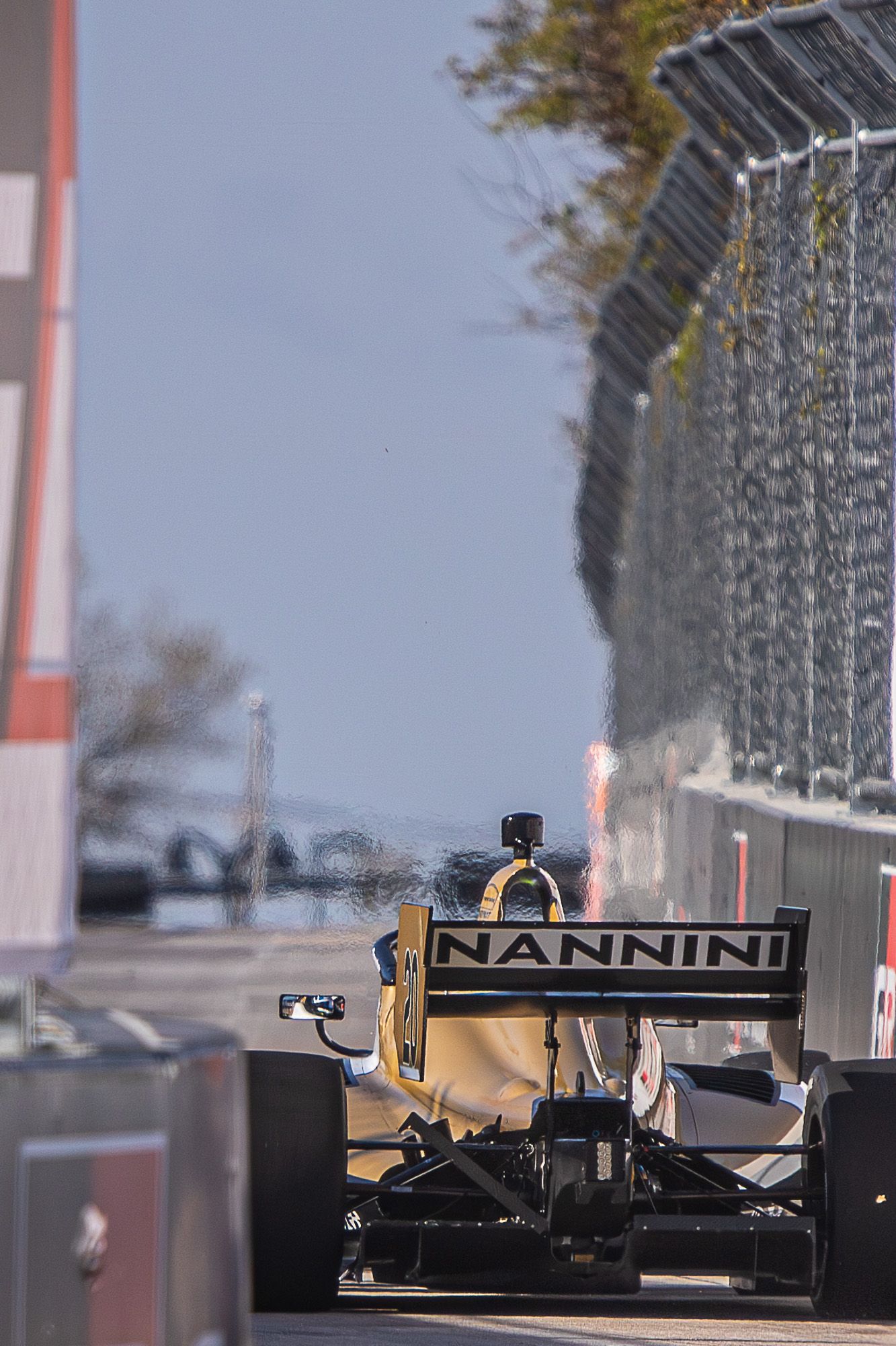 Formula 1 racing car with NANNINI branding speeds along a racetrack with safety barriers visible in the background.