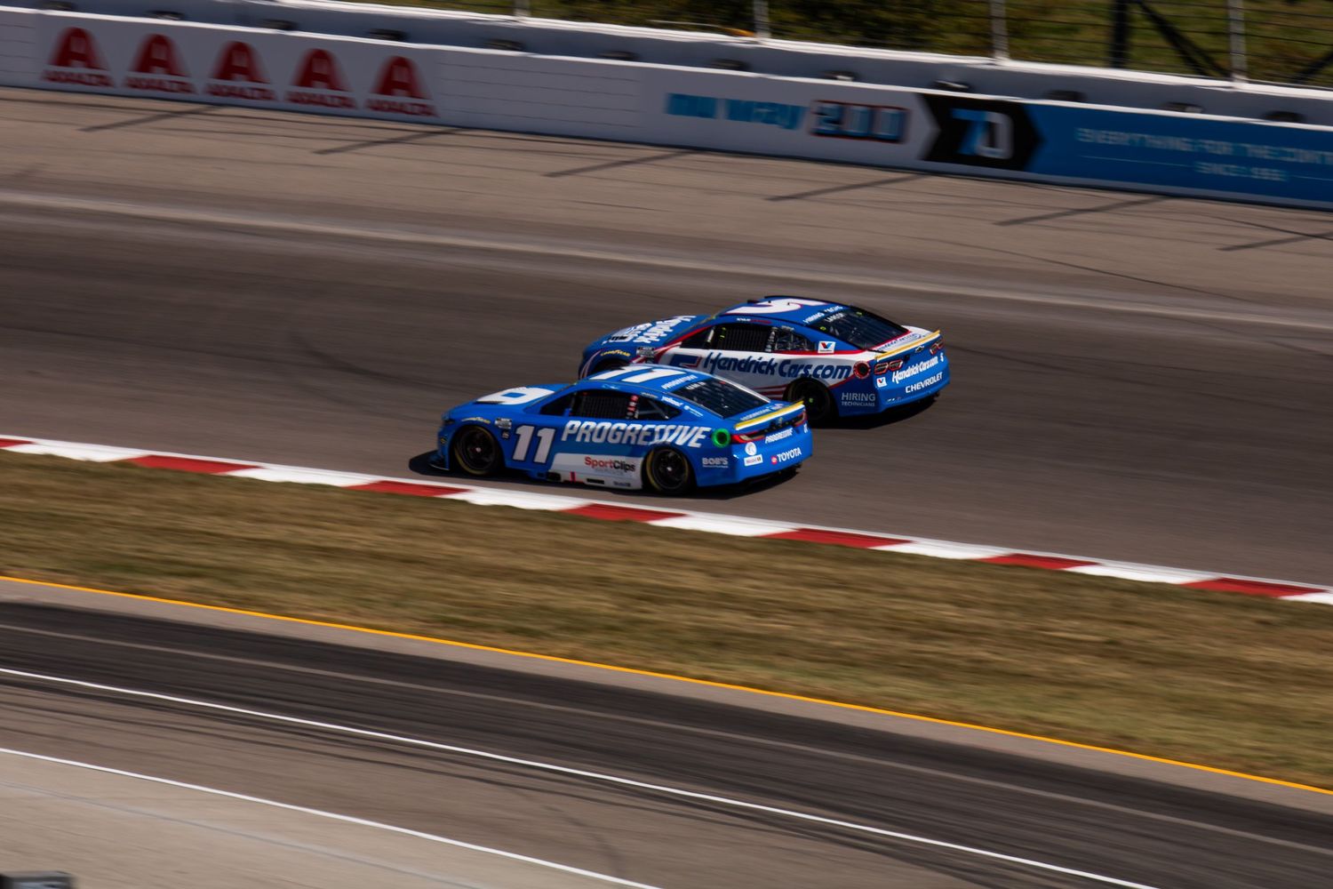 Multiple race cars navigate a curve on the speedway during a NASCAR event.