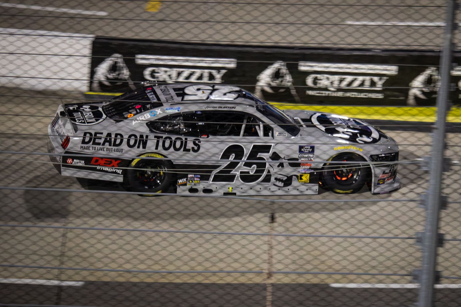 Black and white Dead On Tools NASCAR race car speeds around the track during competition.