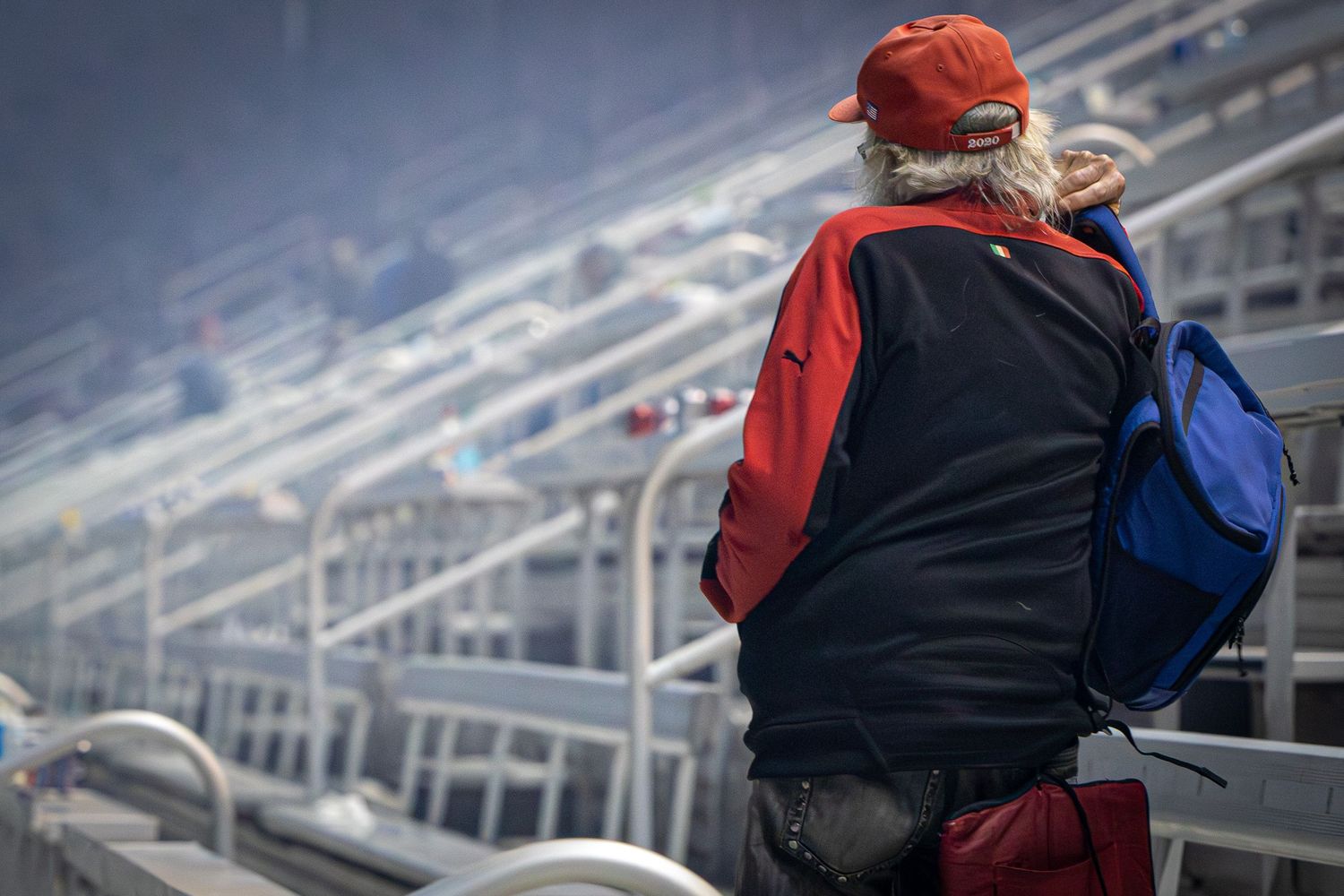 Spectators in red jackets watch from aluminum bleachers at a racing event.