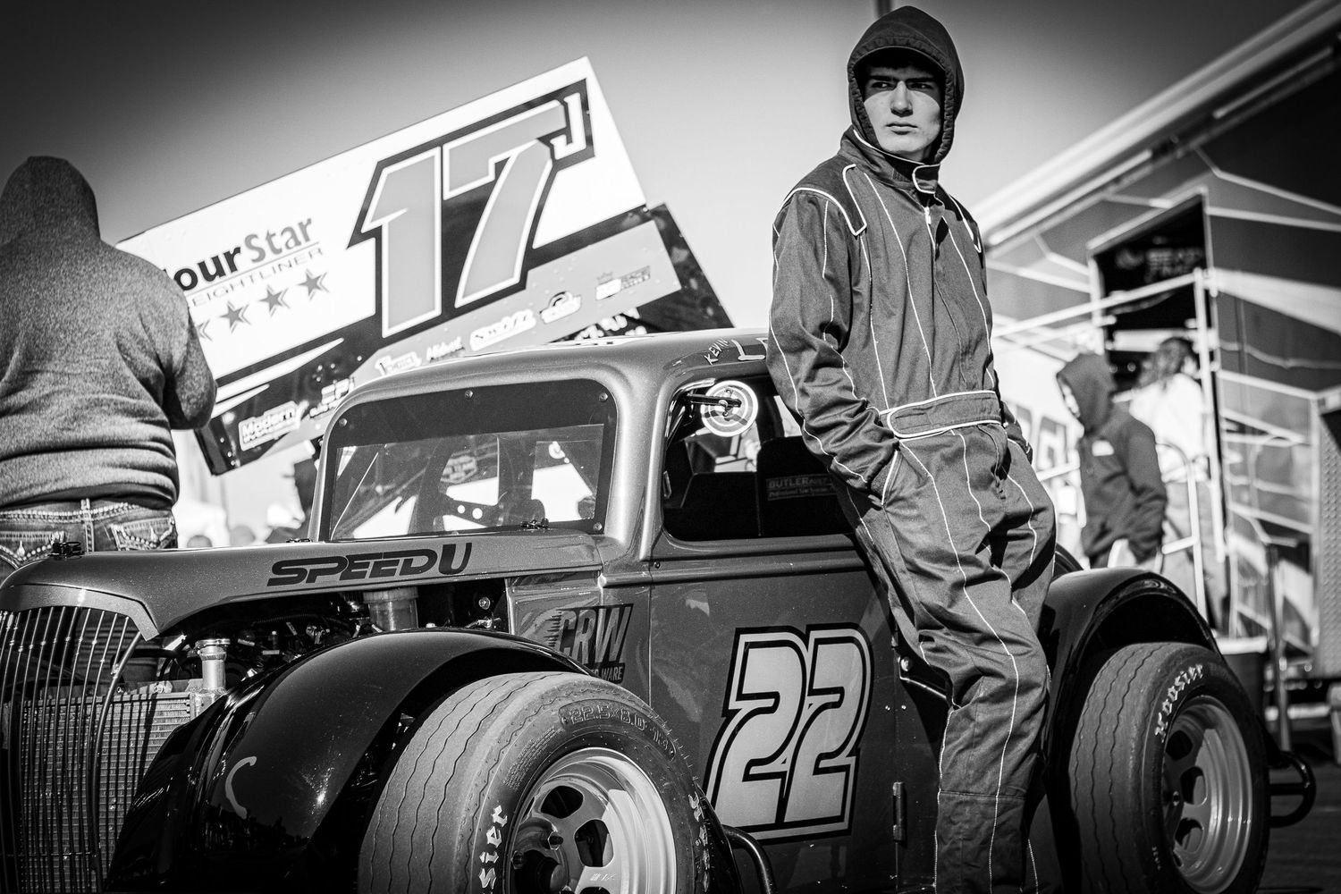 Black and white photo of vintage race cars and crews in a pit lane.