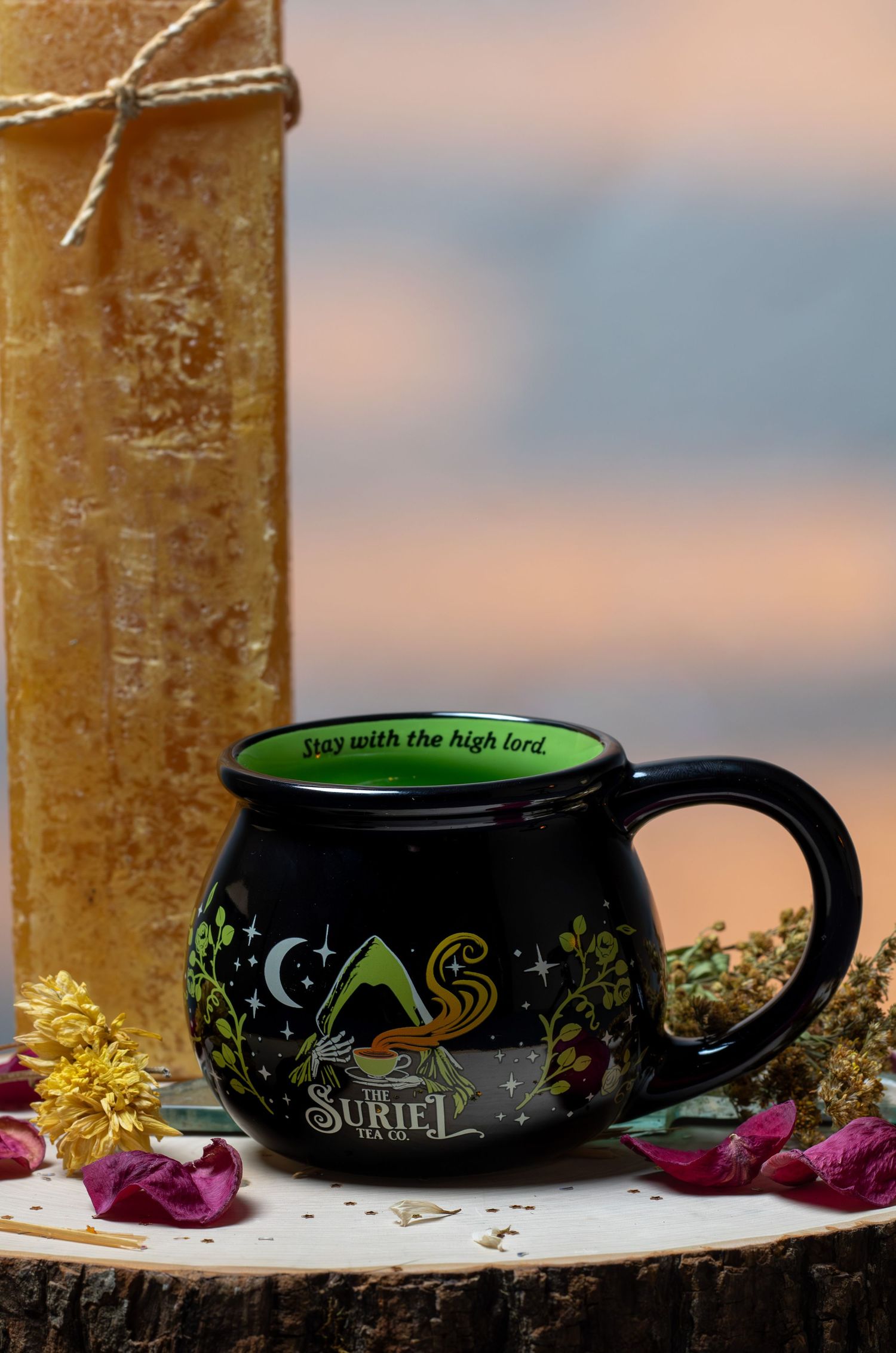 Black cauldron-shaped mug with green interior, floral design, and Stay With The High Lord text by Suriel Tea Co.