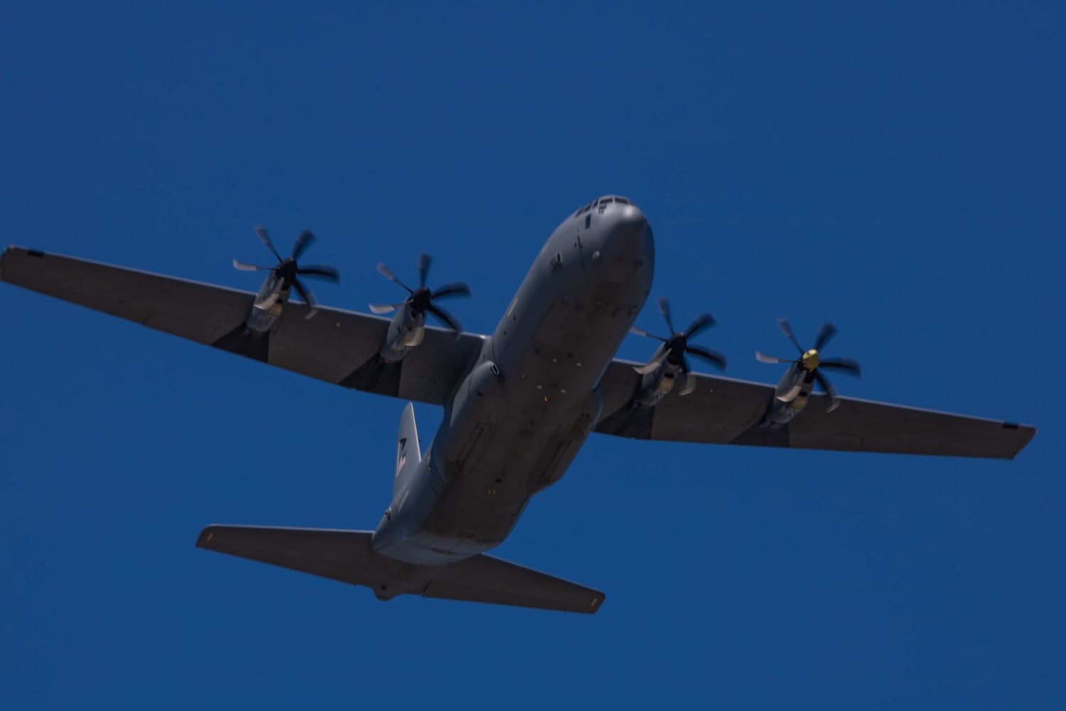 Military cargo plane performing a flyover at a NASCAR race against clear blue sky.