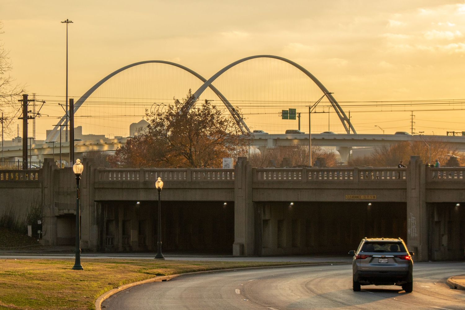 Modern bridge with double arch design silhouetted against a golden sunset sky.