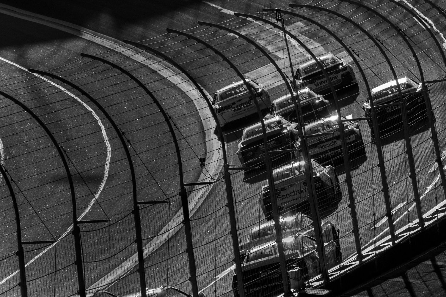 Black and white overhead view of NASCAR stock cars racing along a curved track section.
