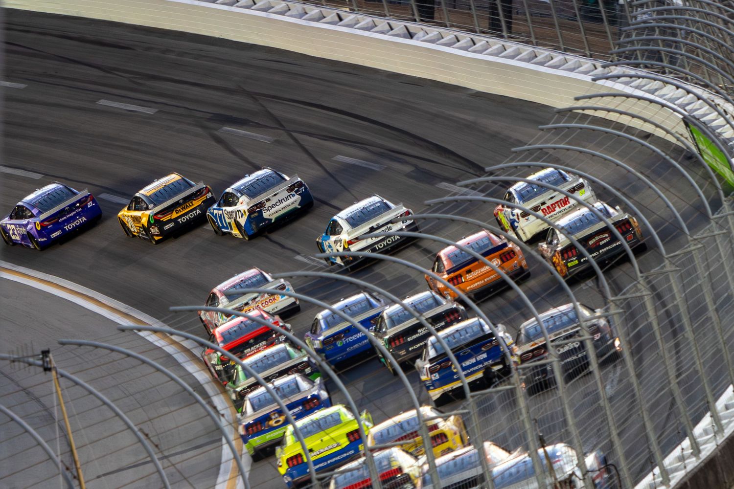 Stock cars racing in close formation around banked turn during a NASCAR event at EchoPark Speedway