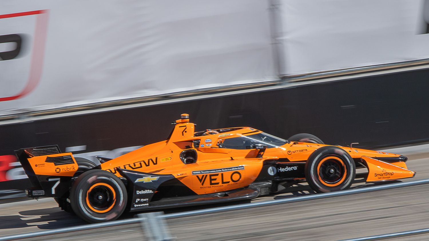 Orange McLaren Formula 1 race car with VELO branding speeds along a race track during competition.