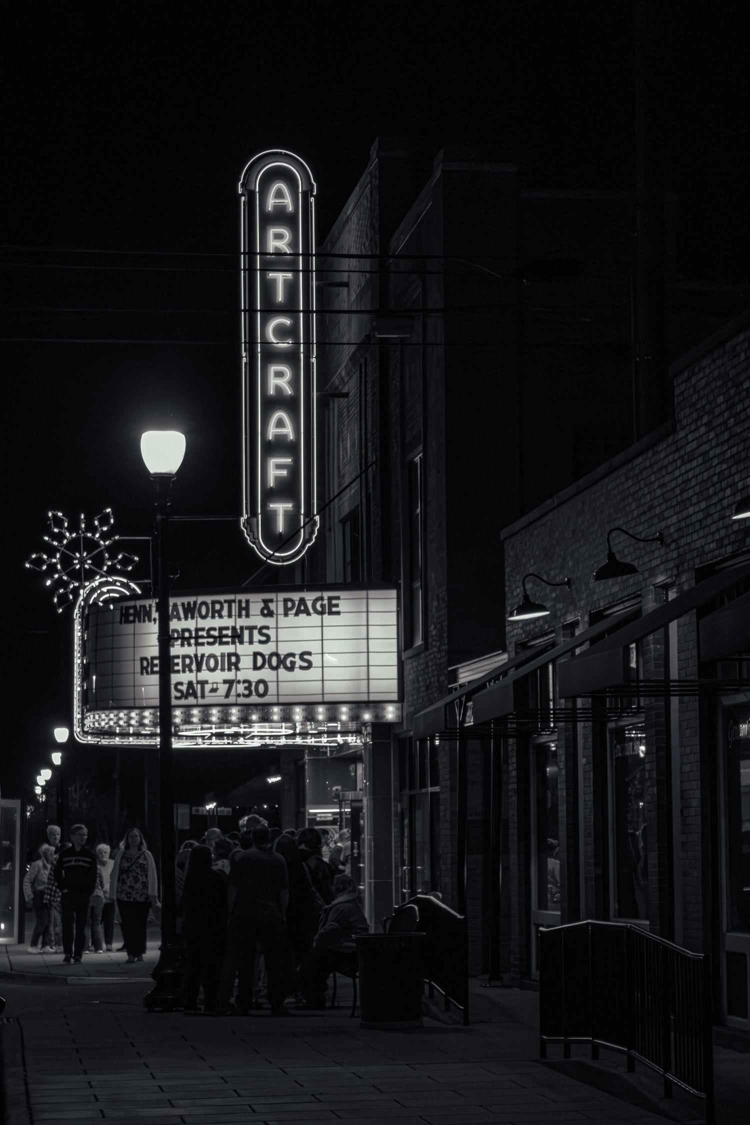 Art Deco movie theater marquee sign glowing at night with crowd gathered outside.