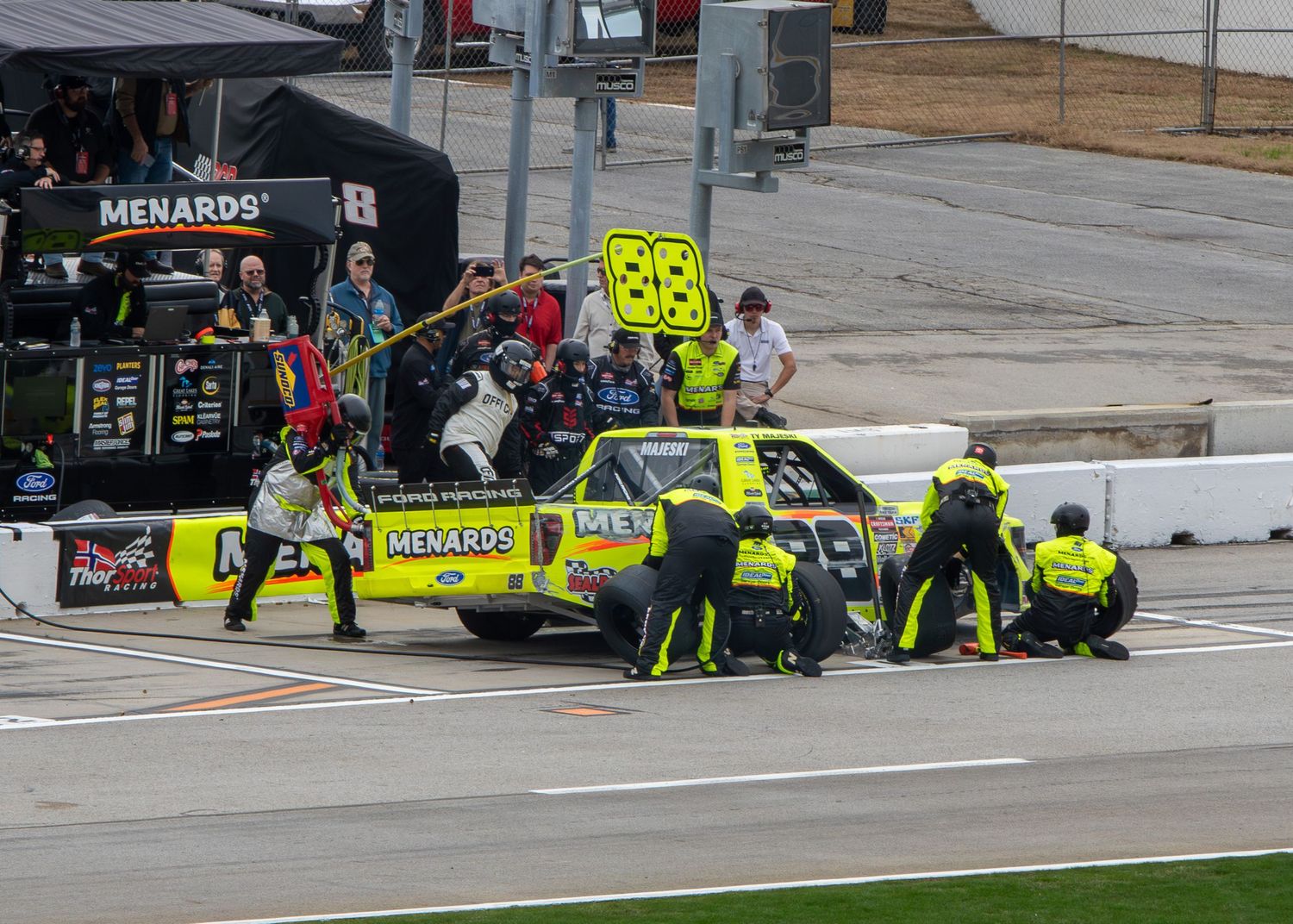 Pit crew members in safety gear perform maintenance on a race car during a pit stop during the Fr8 Racing 208 at EchoPark Speedway on Februa