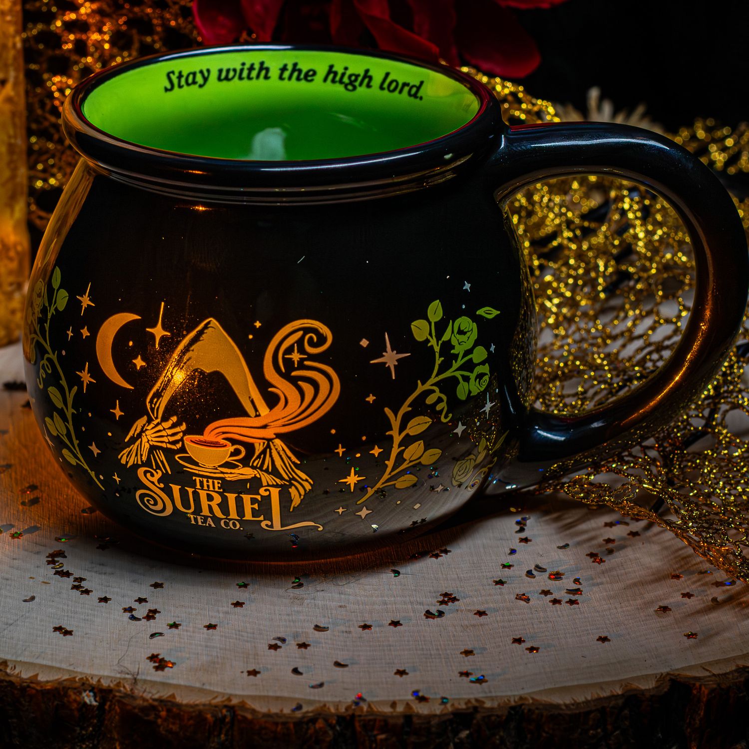 Black cauldron-shaped Suriet Tea Co. mug with gold witch design and green interior reading Stay with the high lord.