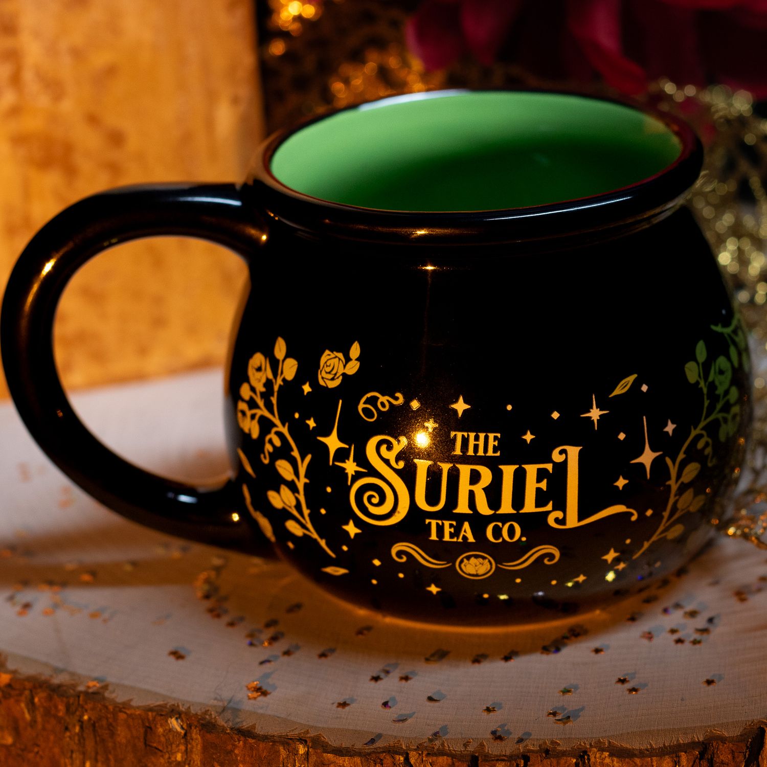 Black cauldron-shaped mug with green interior and gold The Suriel Tea Co. floral design.