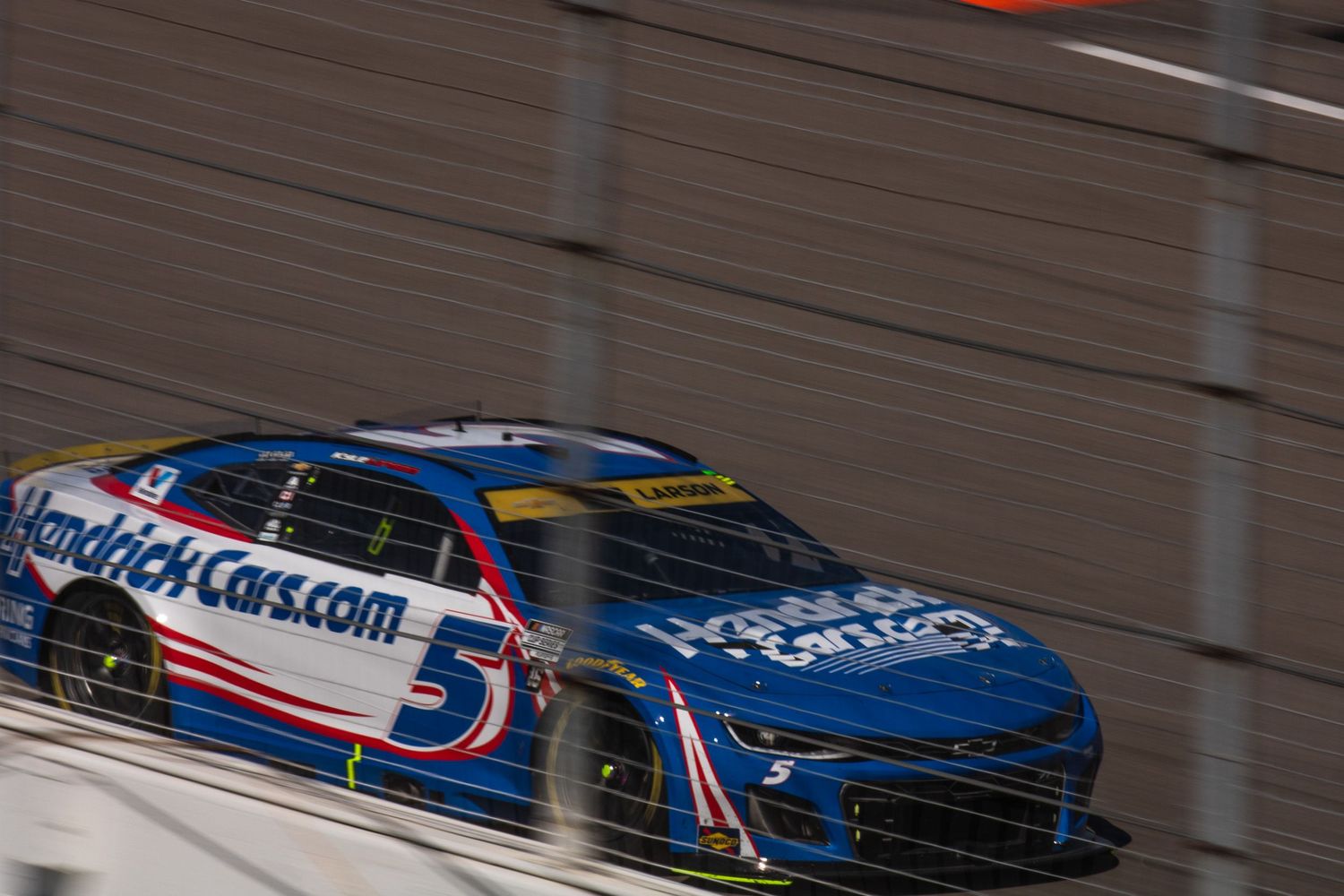 Race cars speed through a banked turn during a professional motorsports competition.