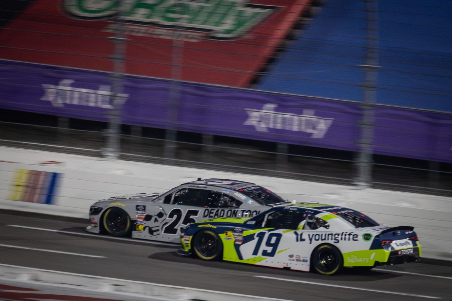 Two NASCAR stock cars race closely together on track during a competitive motorsports event.