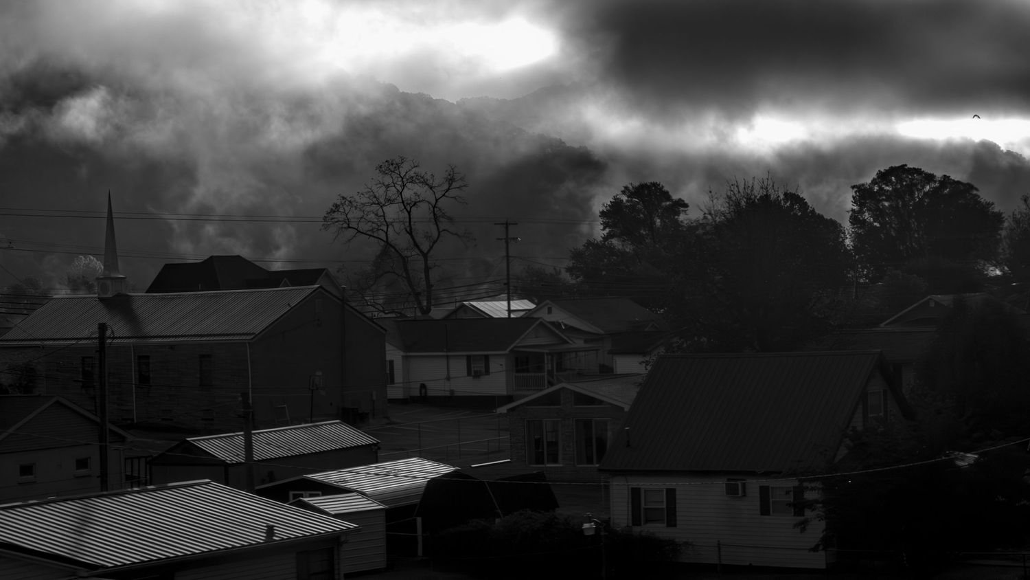 Silhouettes of houses and trees against a dramatic stormy sky at twilight.
