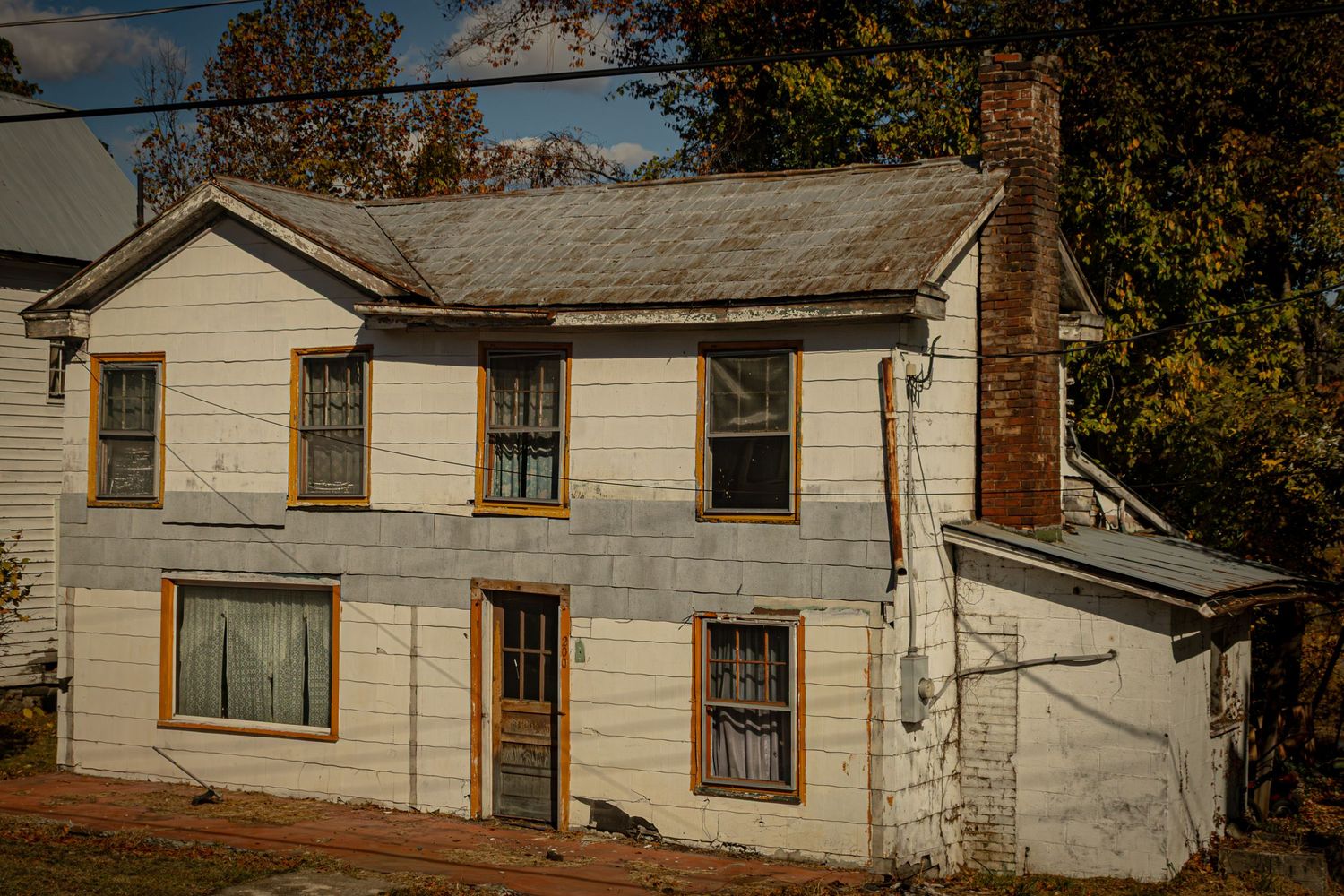 Row of dilapidated rural houses with peeling paint and worn siding against autumn trees.