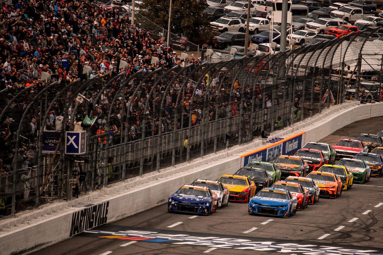 Packed grandstands overlook NASCAR vehicles racing on the track during a major competition.