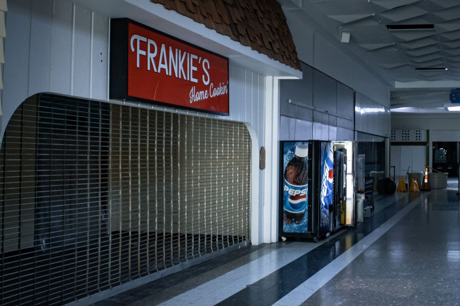Empty mall corridor with closed Frankie's store front and vending machines.