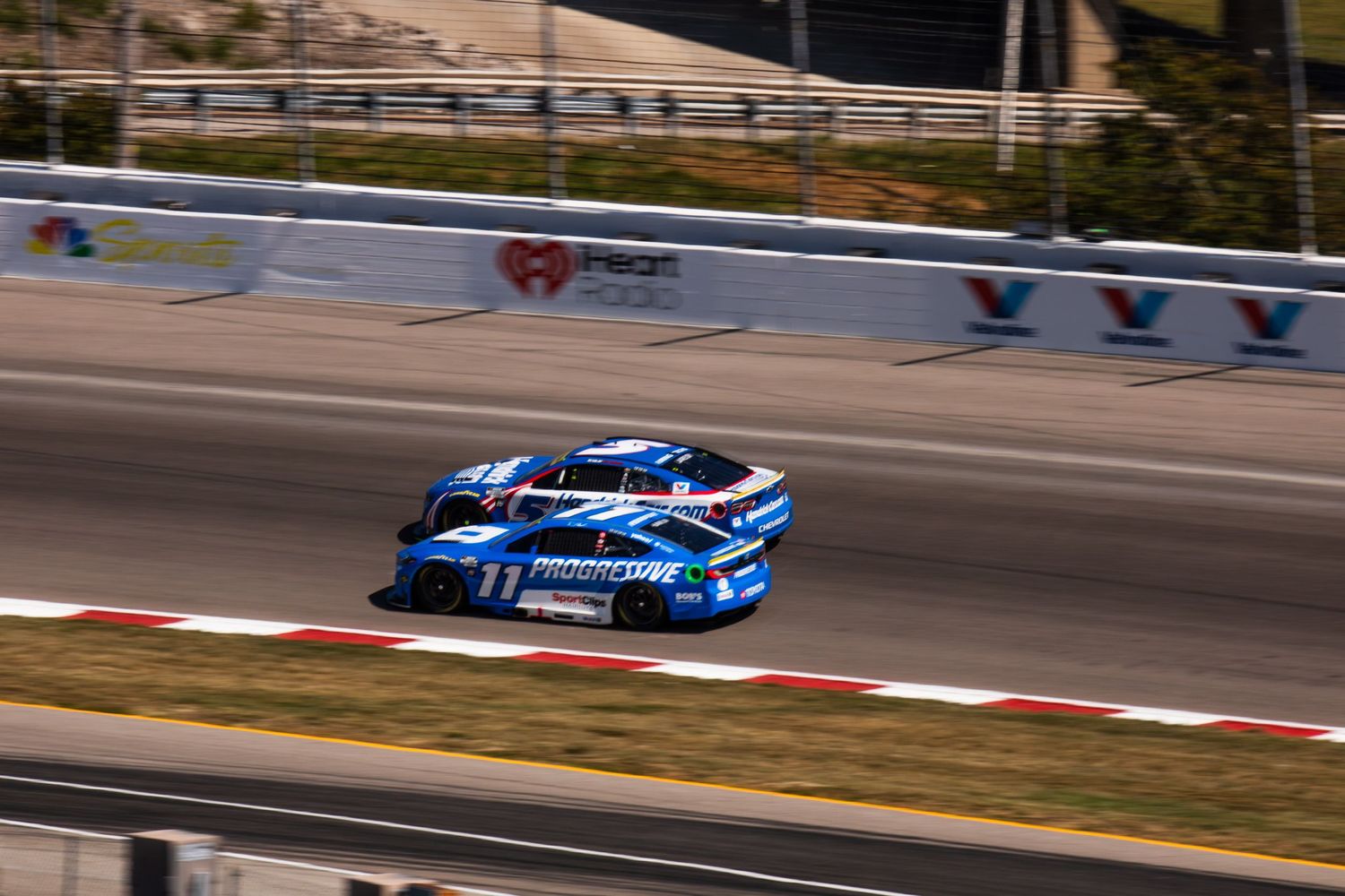 Blue stock car leads the pack around a turn during a NASCAR race competition.