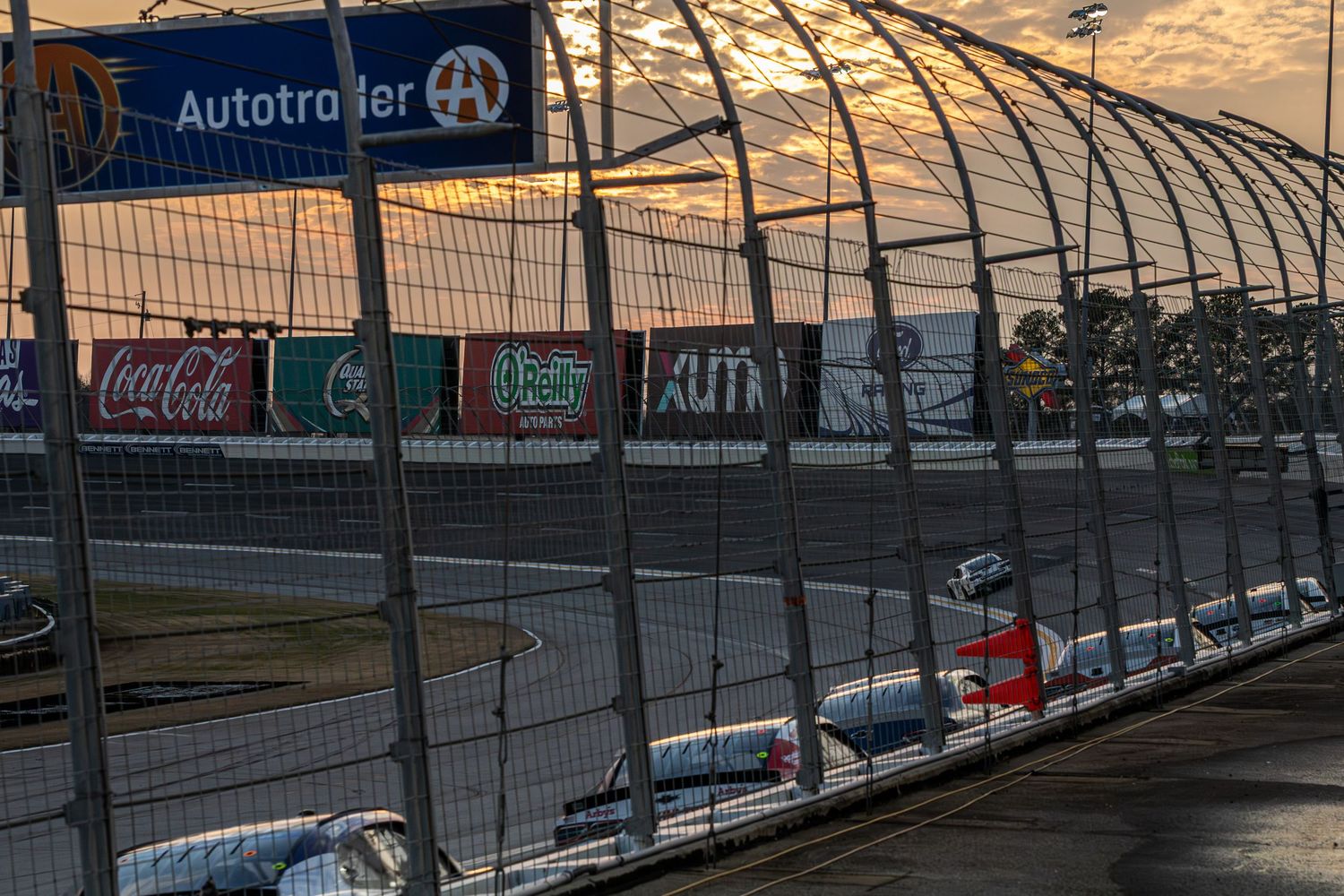 NASCAR race track with safety fencing and advertising boards at sunset showing Autotrader and Coca-Cola signage.