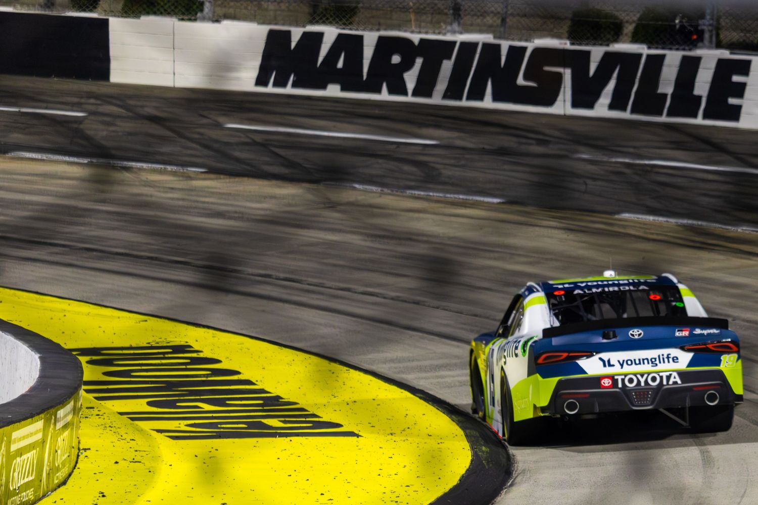 NASCAR stock car races past Martinsville Speedway signage and yellow curbing during competition.