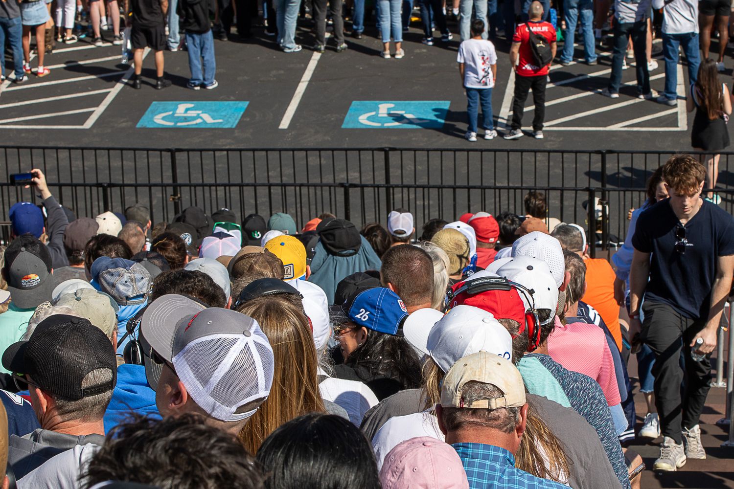 Large crowd of spectators gathered at an outdoor sporting event with blue parking spaces visible in the background.
