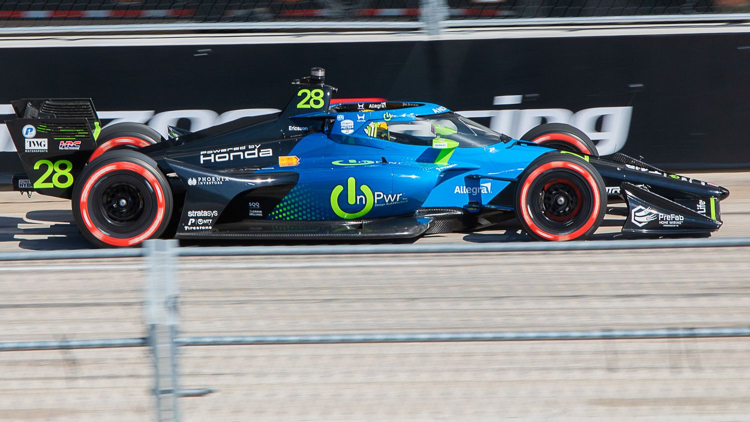 Formula 1 racing car with blue and black livery speeds along track with red-walled tires during competition.