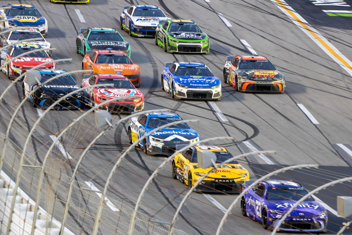 Colorful NASCAR vehicles compete in tight pack racing during an EchoPark Speedway event.