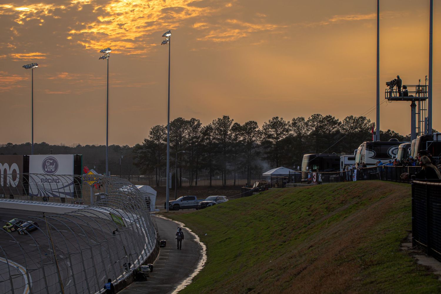 Dramatic orange sunset sky over a racing track with silhouetted grandstands.