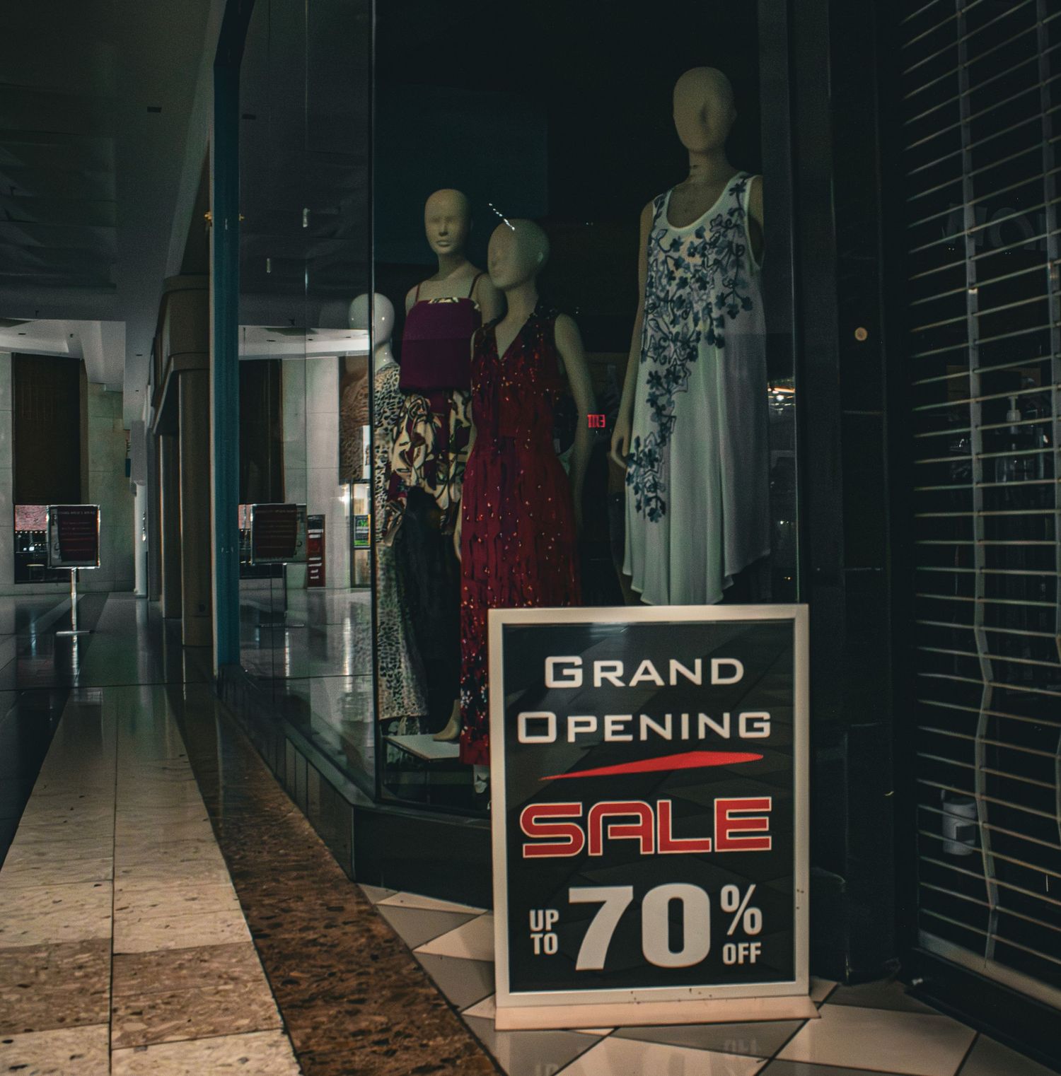 Retail store window display with mannequins and 70% off grand opening sale sign.