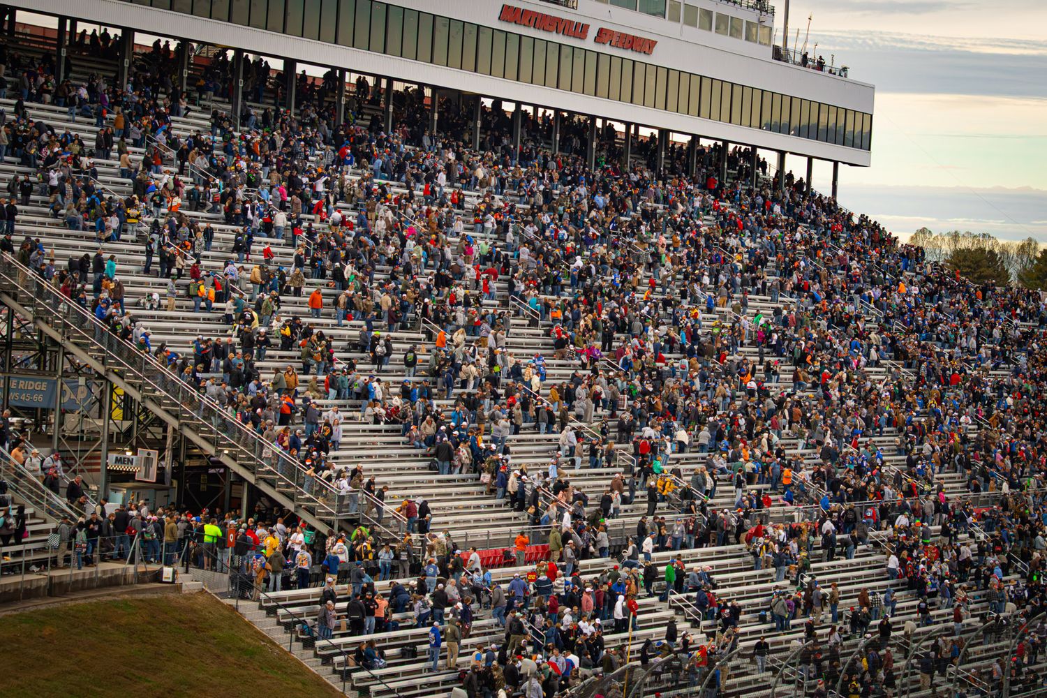Stadium bleachers filled with spectators during a sporting event at sunset.