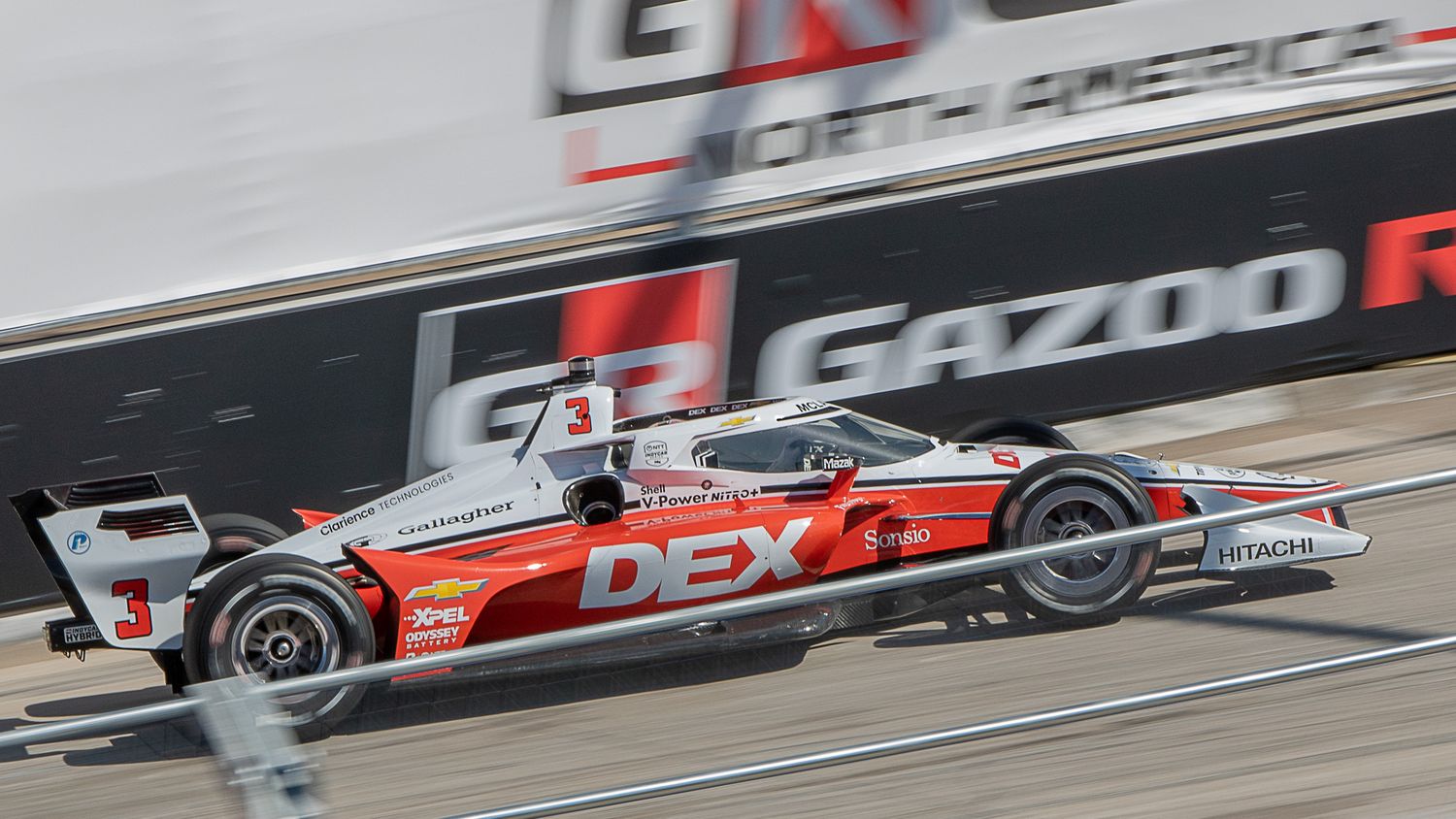 Multiple racing cars speed around a racetrack during an IndyCar Series competition event.