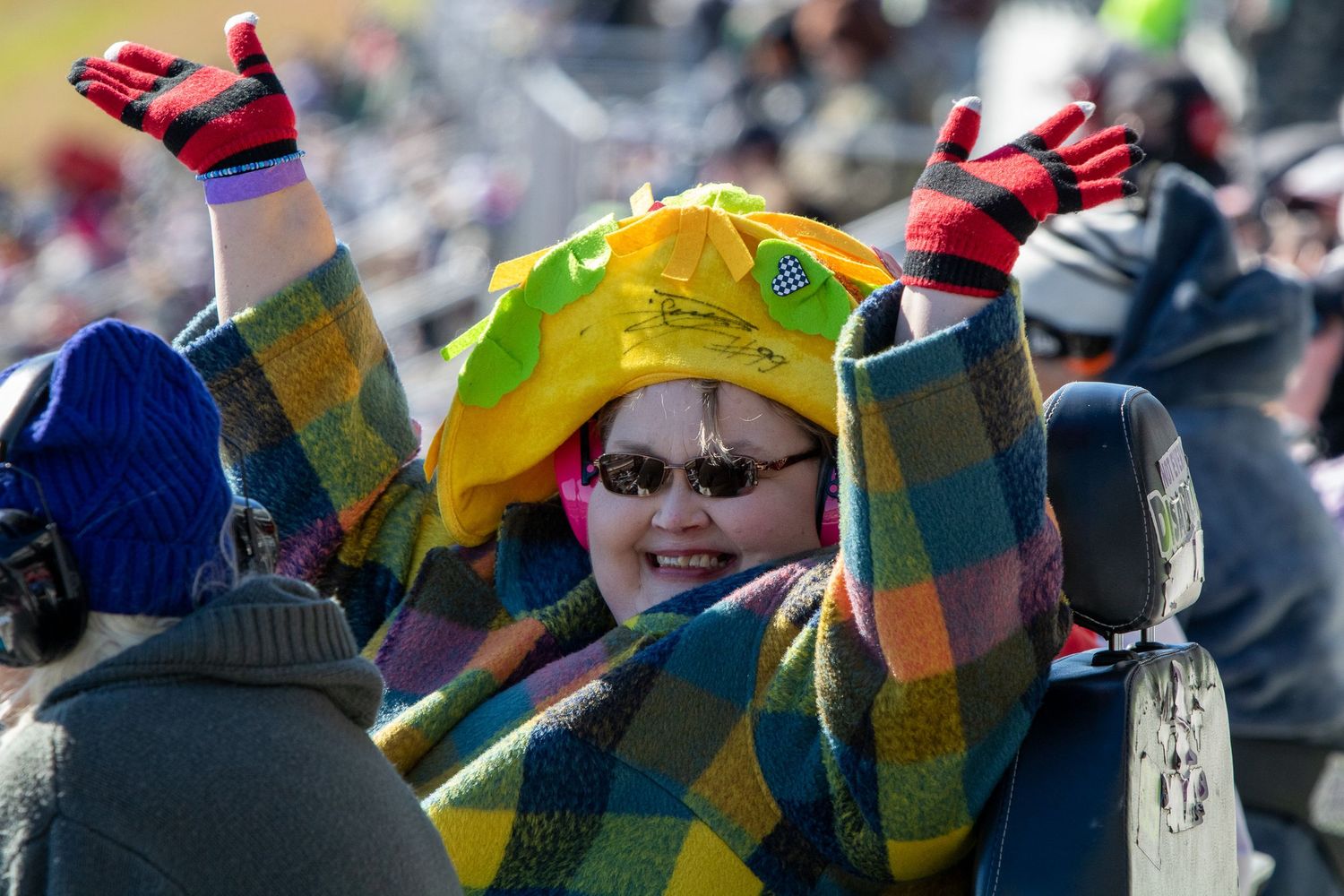 Colorful flags and winter clothing fill the crowded spectator stands at a racing event.