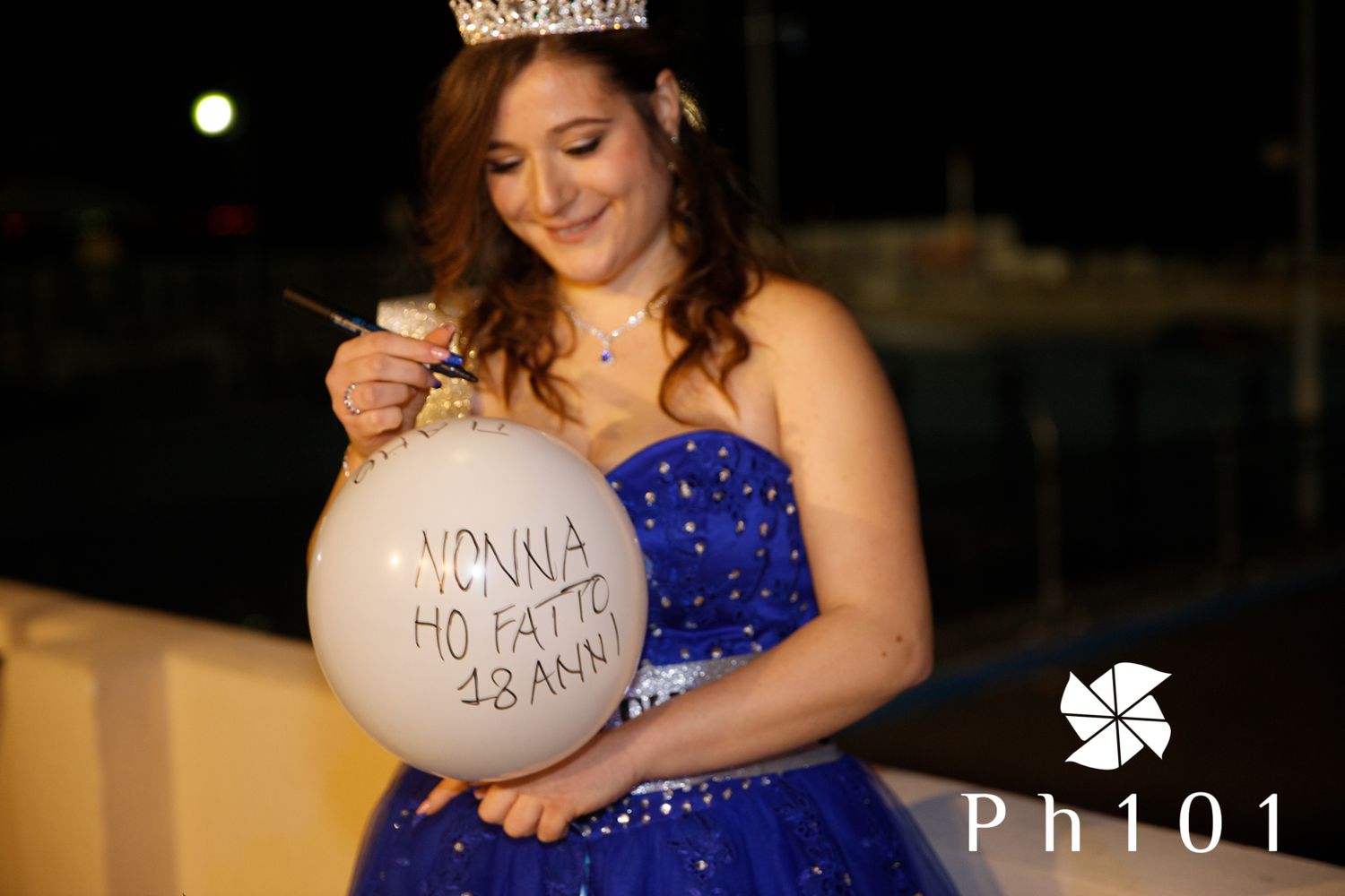 Woman in a royal blue evening gown poses elegantly during a nighttime photoshoot.