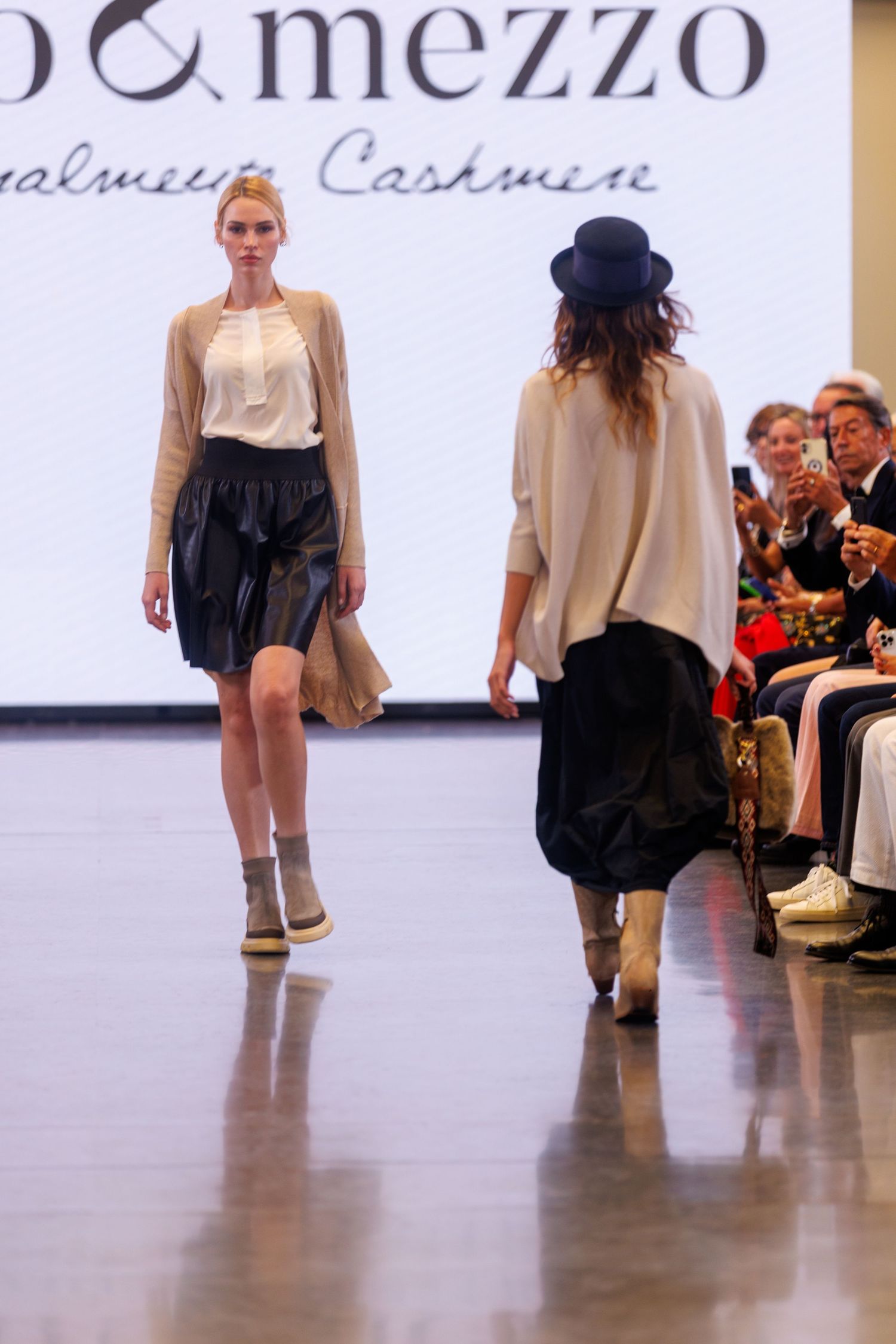 Models showcase casual clothing collection on a minimalist white runway with audience visible.