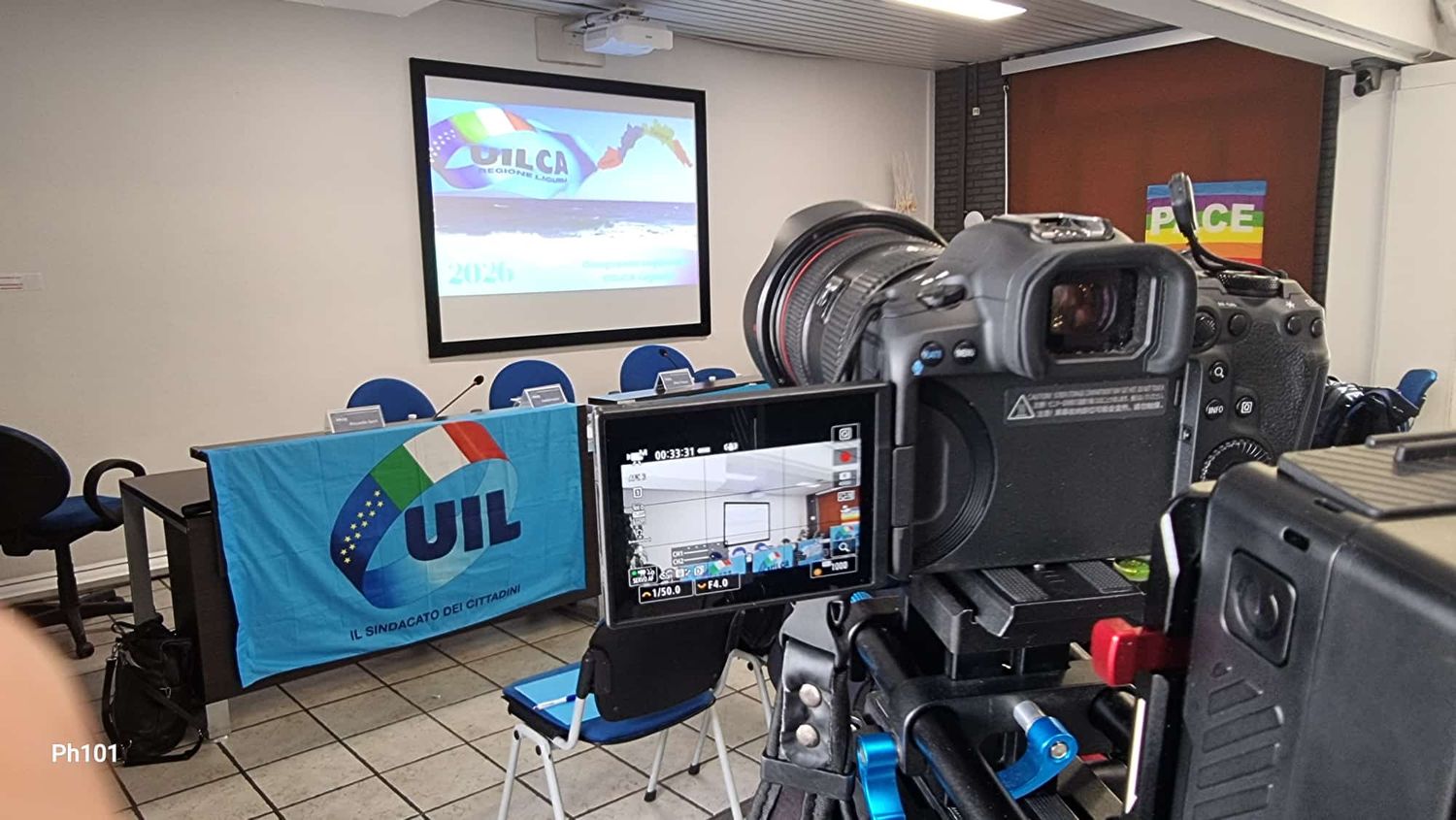 Camera setup filming a UIL union meeting room with blue flag, chairs, and presentation screen.