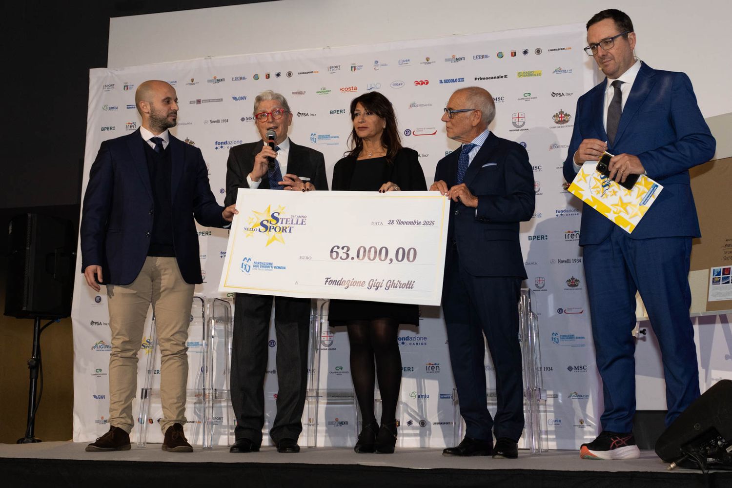 Group of people standing on stage at formal presentation event with large check display.