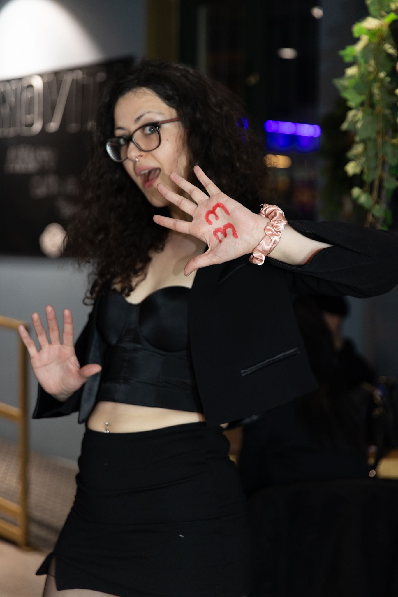 A person in black clothing makes playful expressions and hand gestures in a sequence of photos at a dimly lit venue.