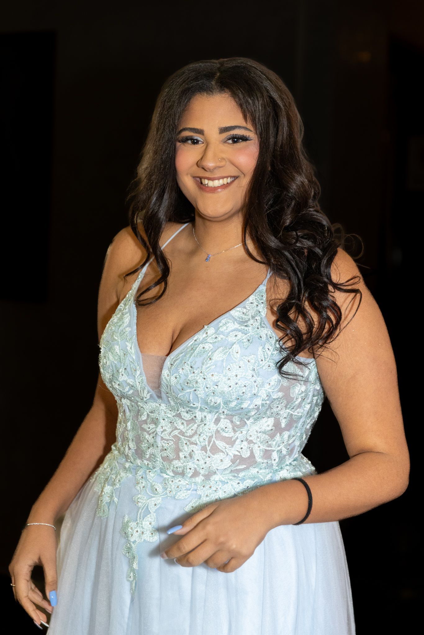 Woman wearing white lace gown with beaded bodice poses against dark background.