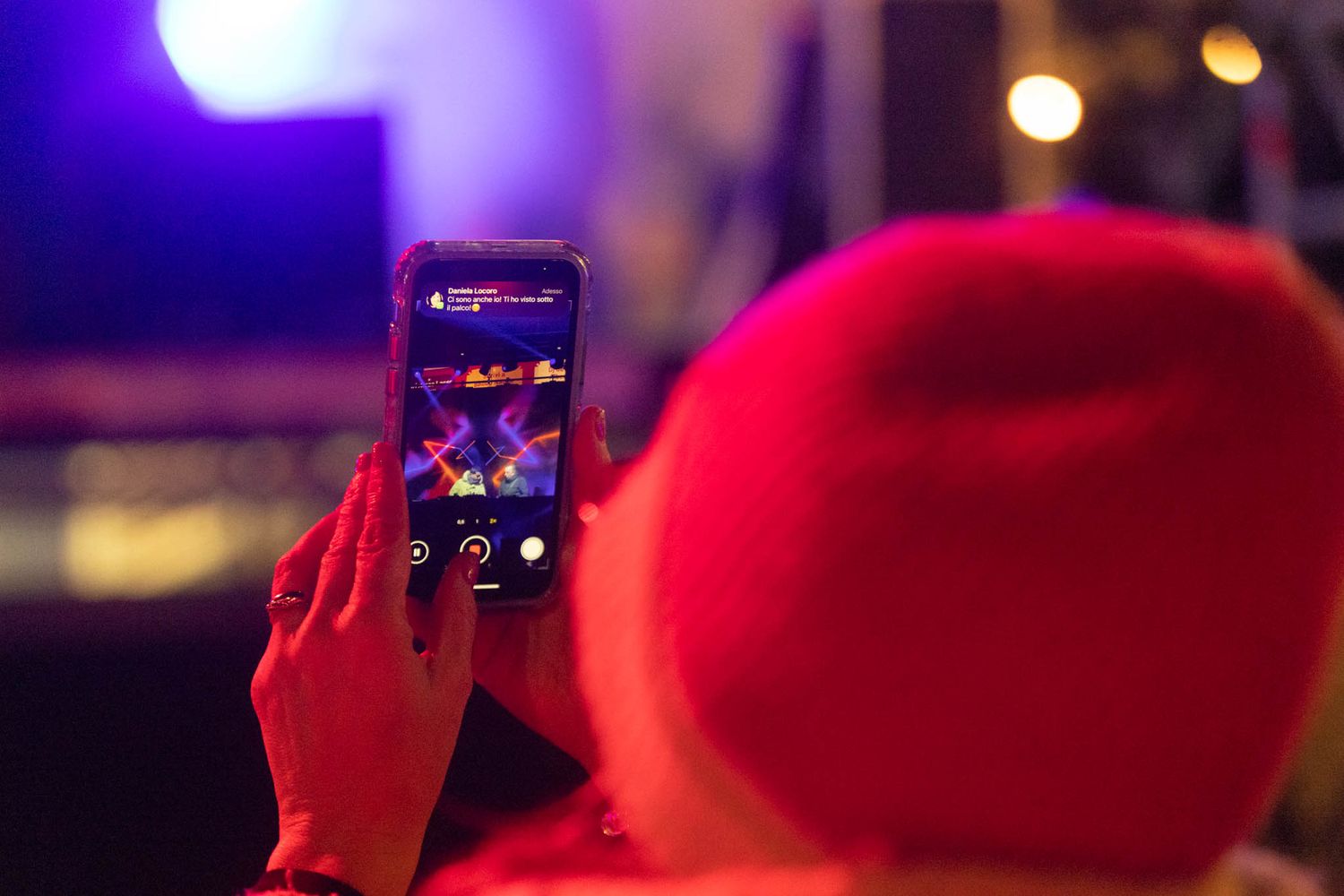 Concert crowd illuminated by vibrant purple and red stage lighting during a live performance.