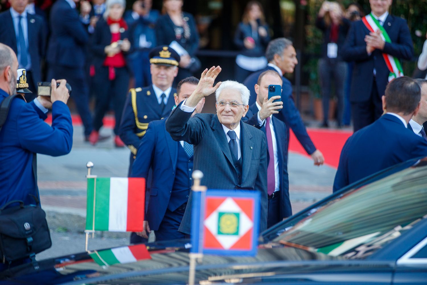 Official ceremony with Italian flags and formal vehicles in attendance.