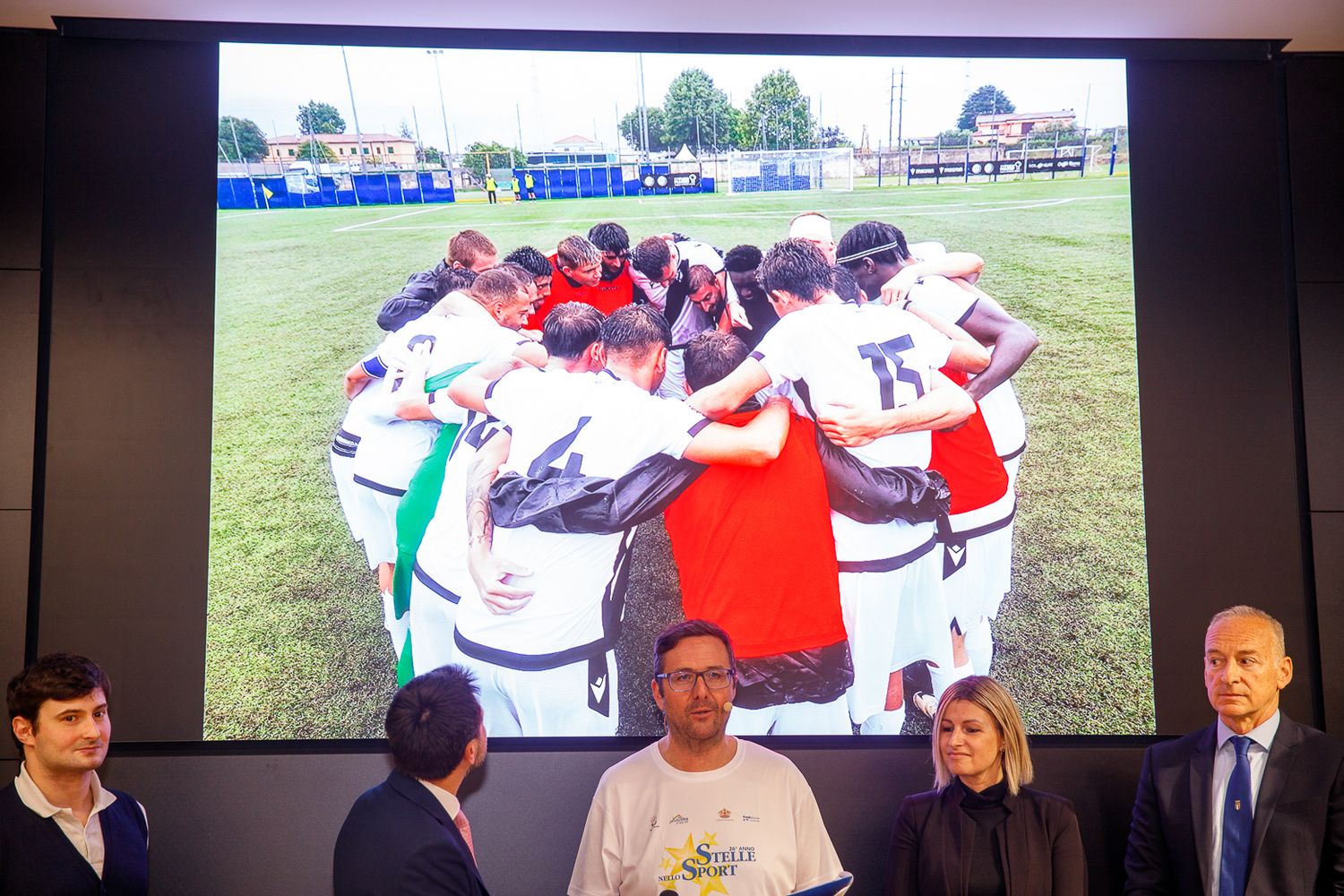 Sports team gathering on a field shown on large display screens.
