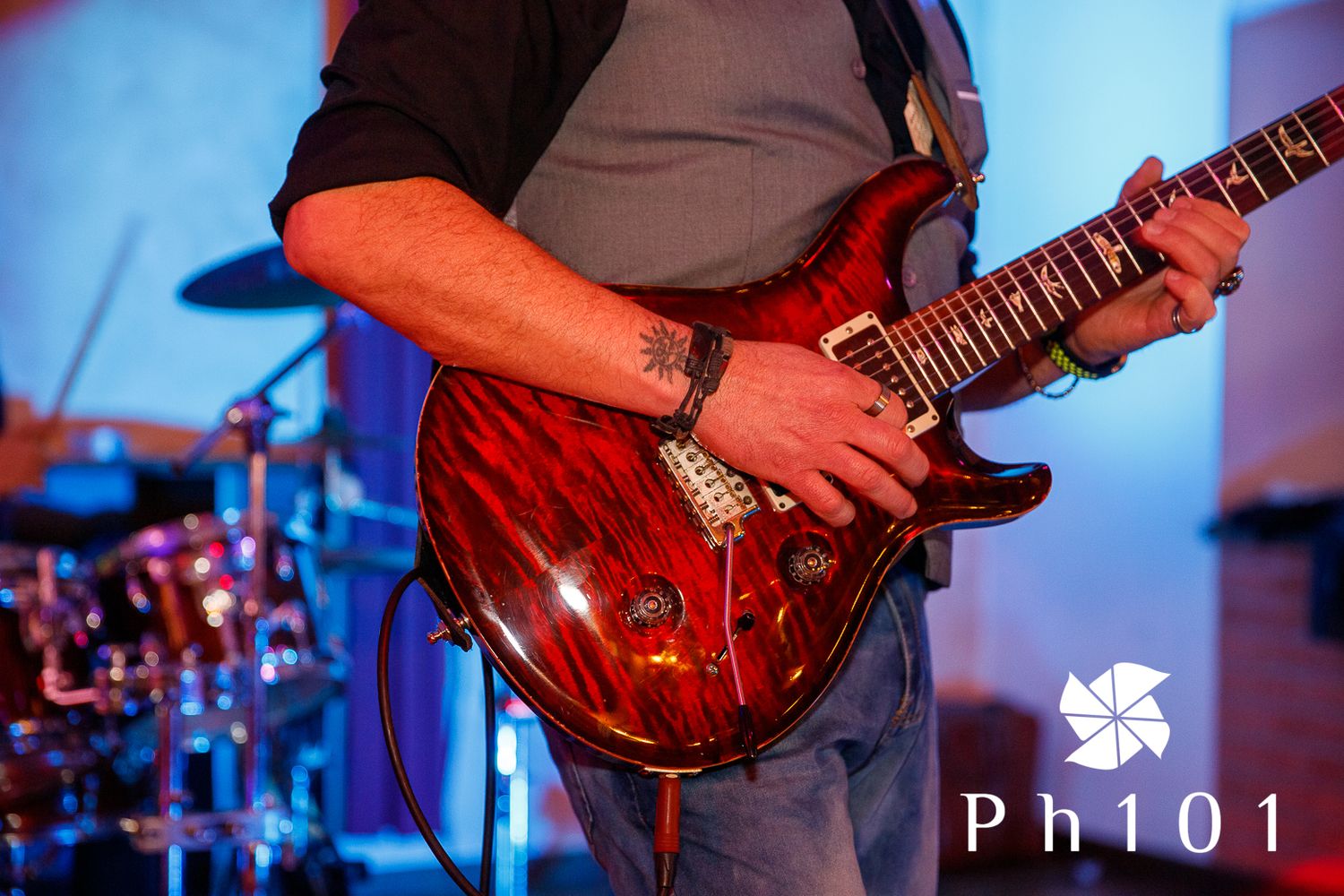 Musician playing a red electric guitar on stage with blue lighting effects.