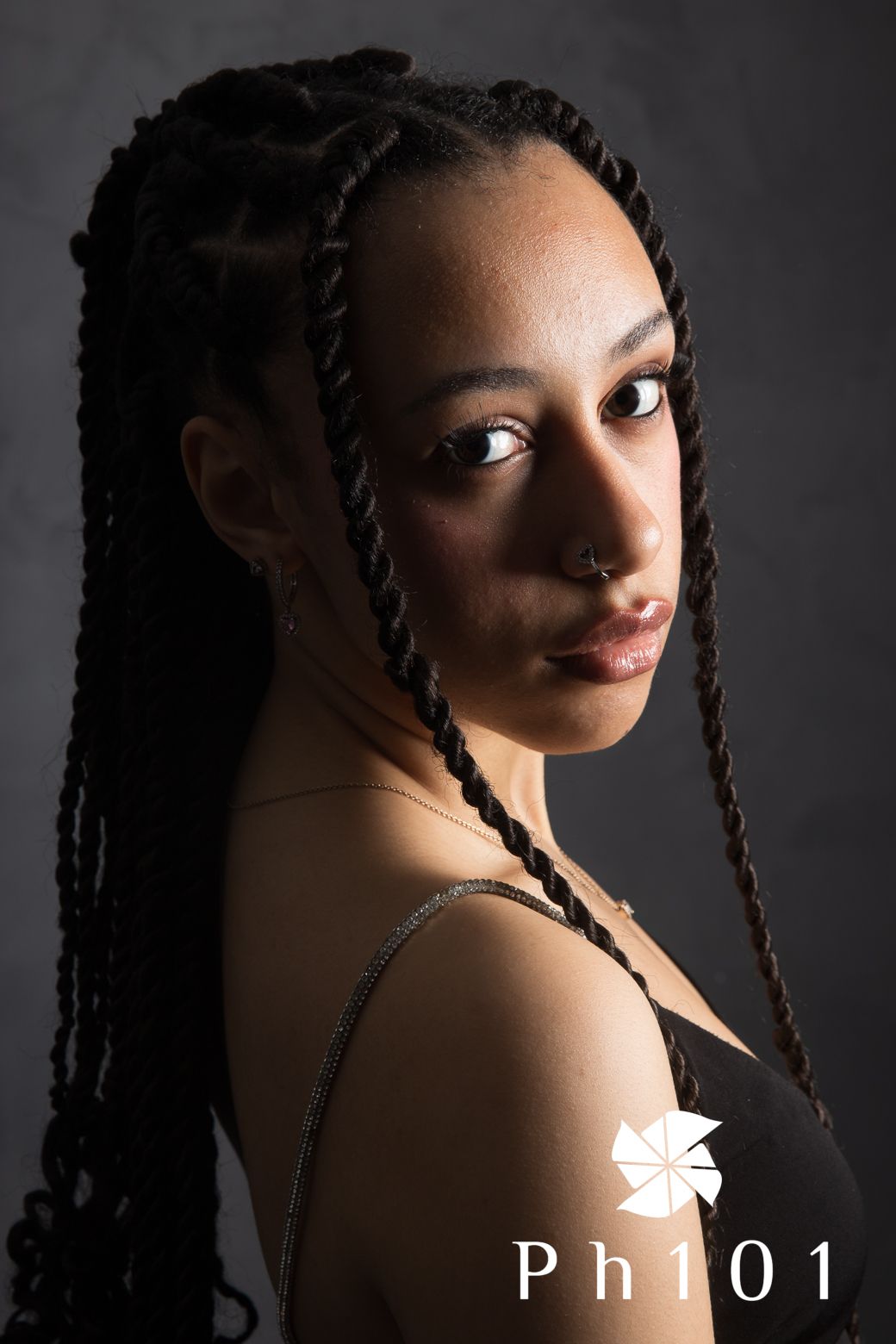 Elegant studio portrait with braided hairstyle against dark background.